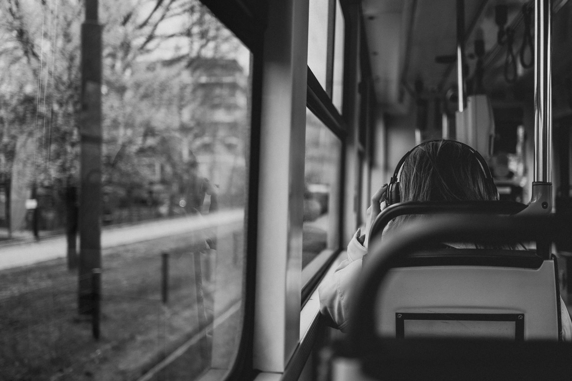 A traveler enjoys music while commuting by bus, captured in a black and white perspective.
