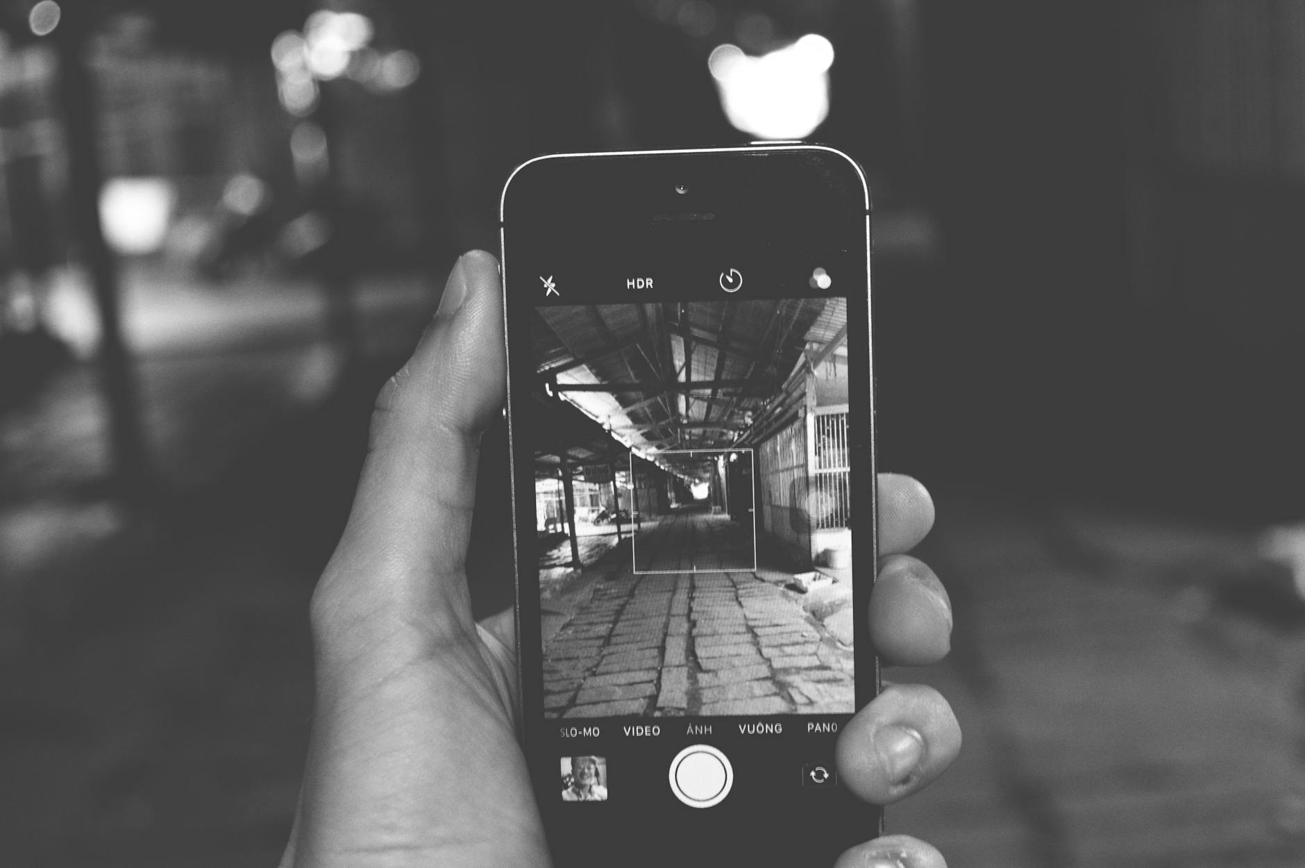A smartphone held in hand displays a monochrome photo of an indoor setting.