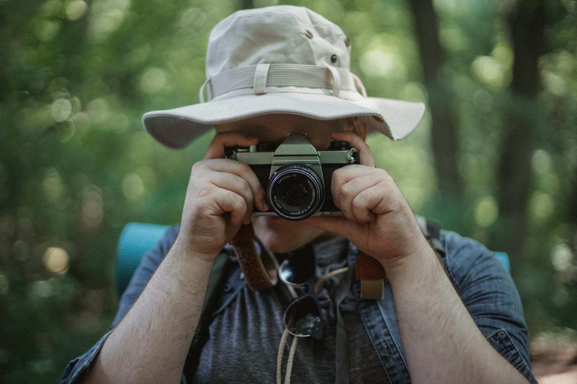 Unrecognizable male traveler taking photo on camera during trip in summer forest on weekend