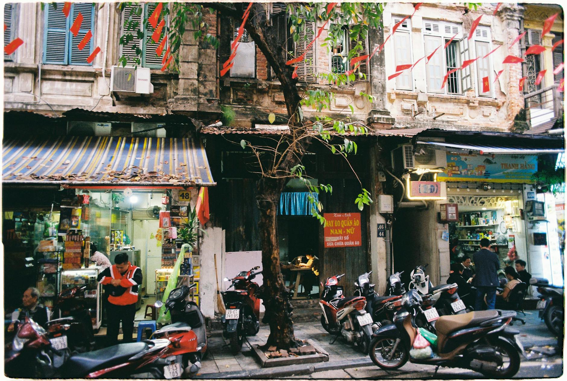 Bustling Hanoi street scene with motorbikes, shops, and colorful decorations.
