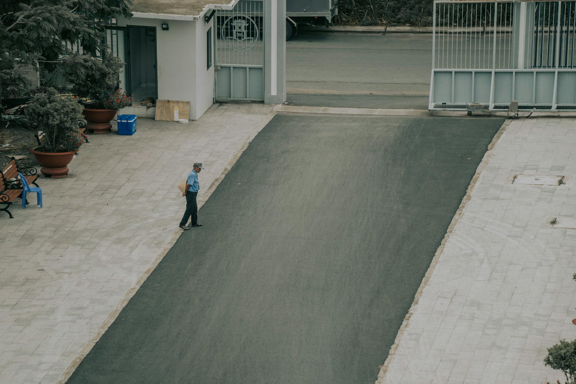 Aerial view of a man walking on a paved driveway lined with potted plants and a gate.