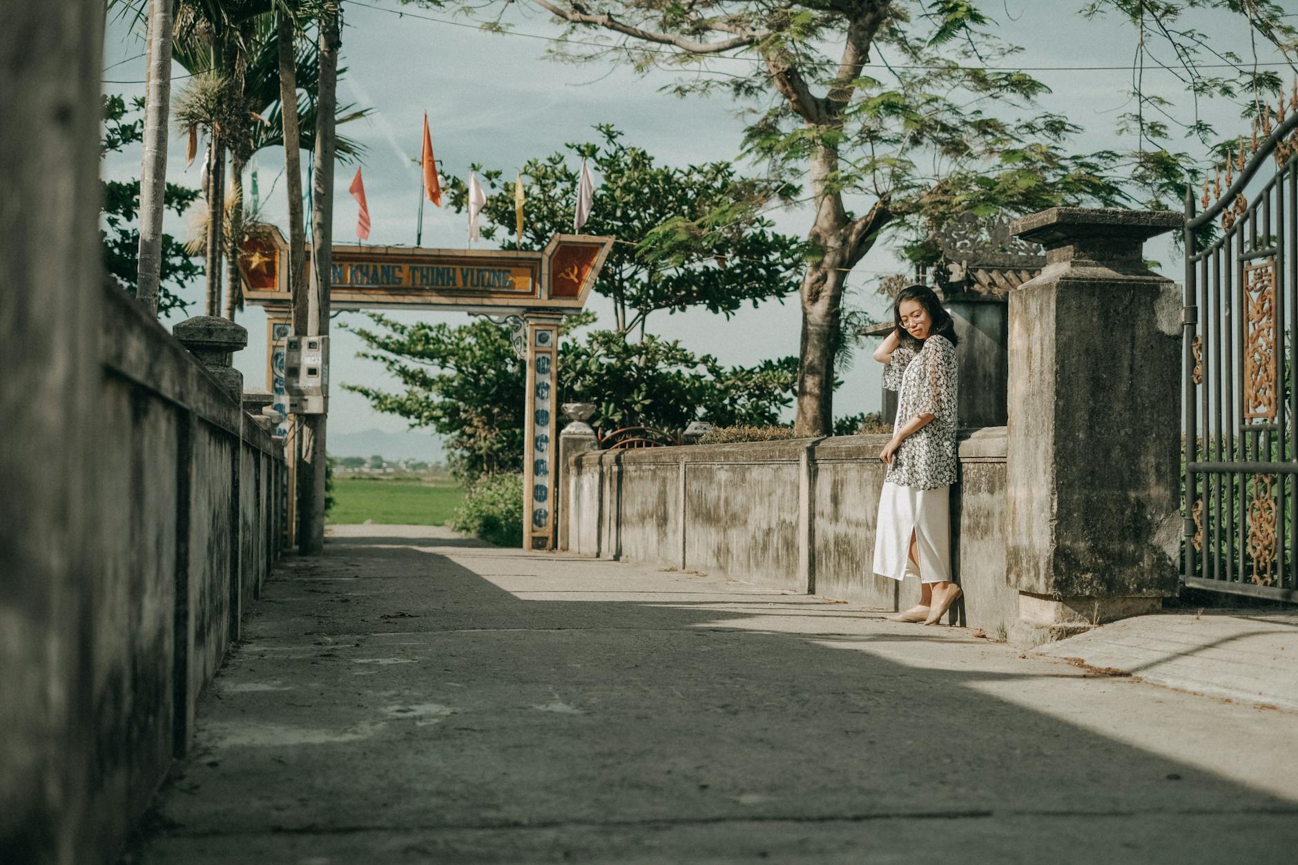 A woman stands by a traditional village gate under a clear sky, embodying peace and cultural heritage.