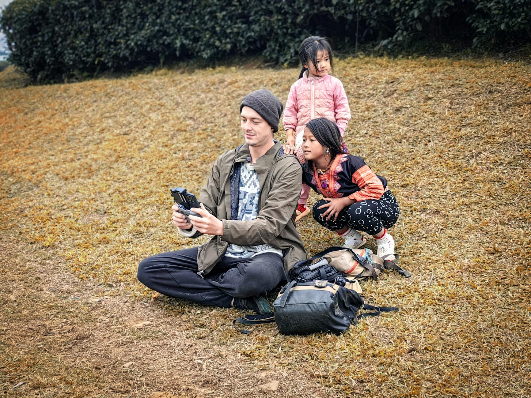 Man showing drone remote control to two children on a grassy hill in Vietnam.
