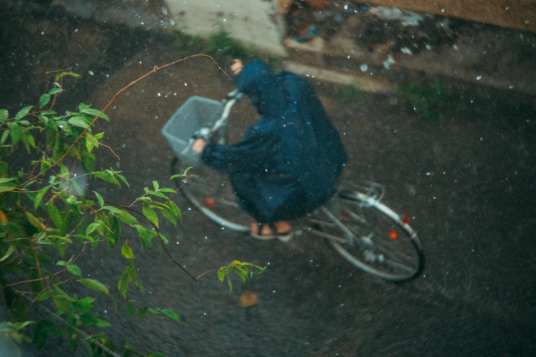 Person cycling in rain wearing a raincoat, captured from above, showcasing motion and weather.
