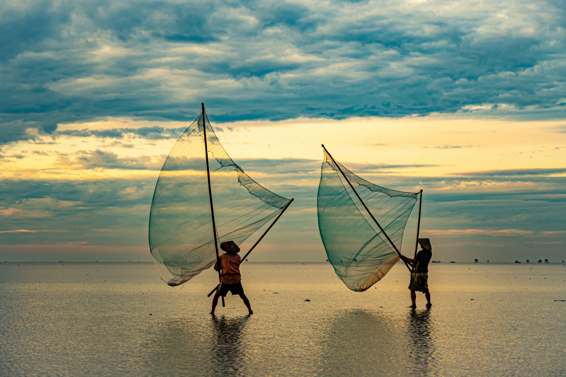 Two fishermen in Thai Binh, Vietnam casting nets at sunrise, capturing serene coastal life.
