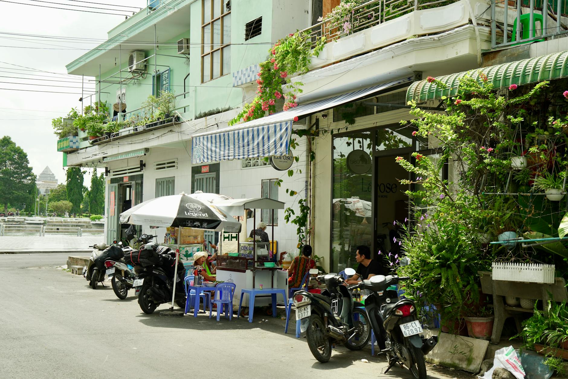 Street-side food stall with motorbikes, vibrant plants, and urban setting, perfect for capturing local vibe.