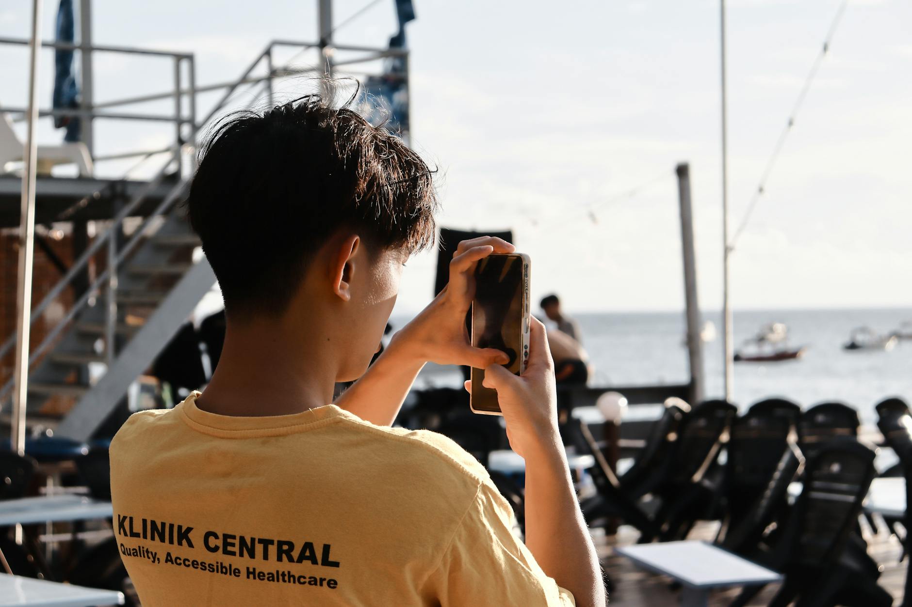 A young man takes a beachside photo with his smartphone, enjoying a sunny day.