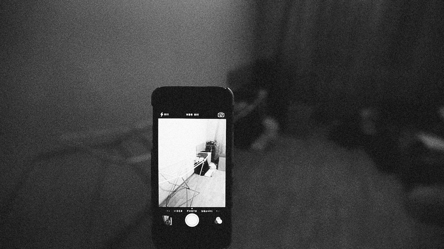 Artistic grainy black and white image of a smartphone capturing a room scene.