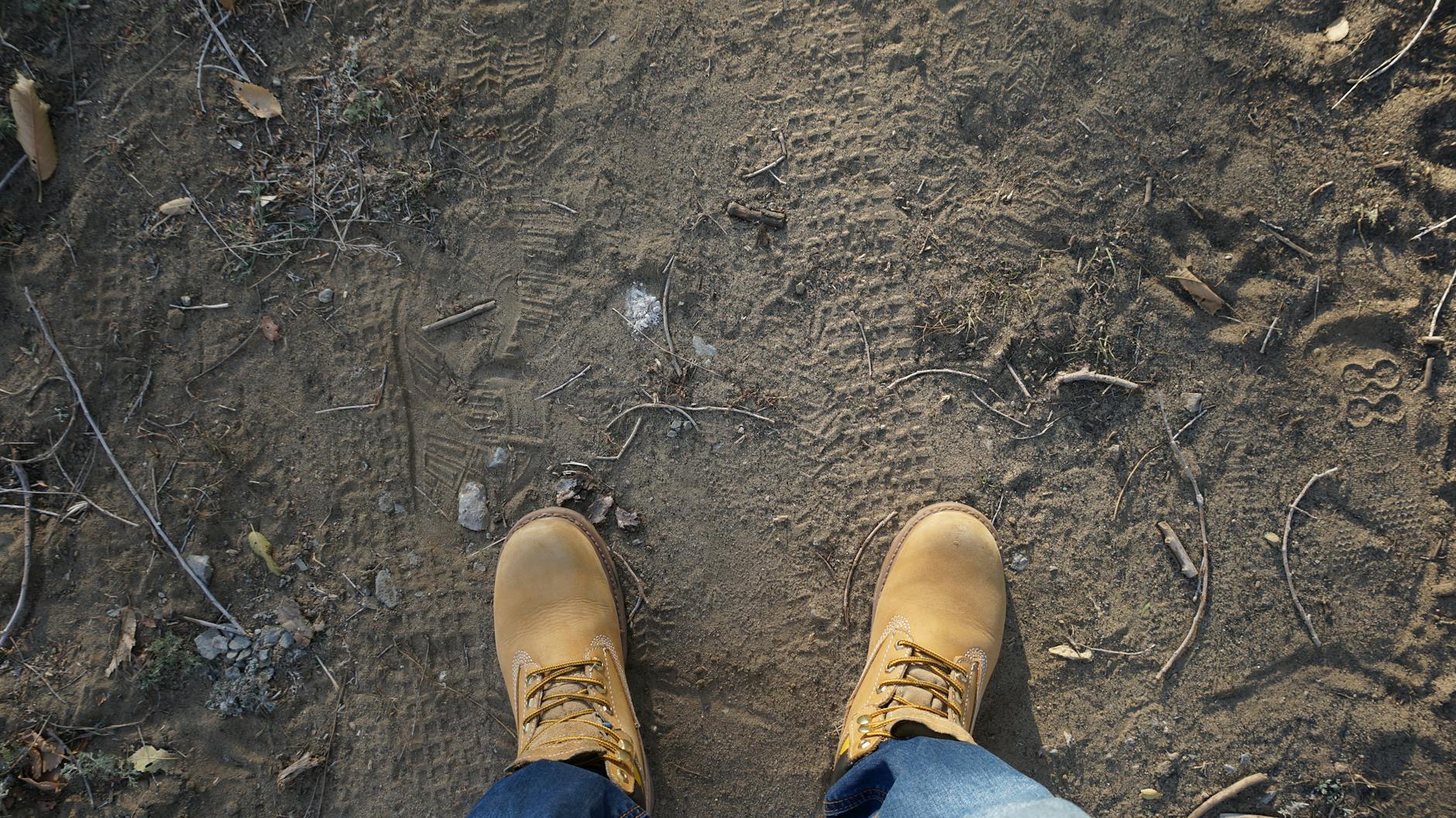 A pair of brown hiking boots on a rugged outdoor trail with footprints.