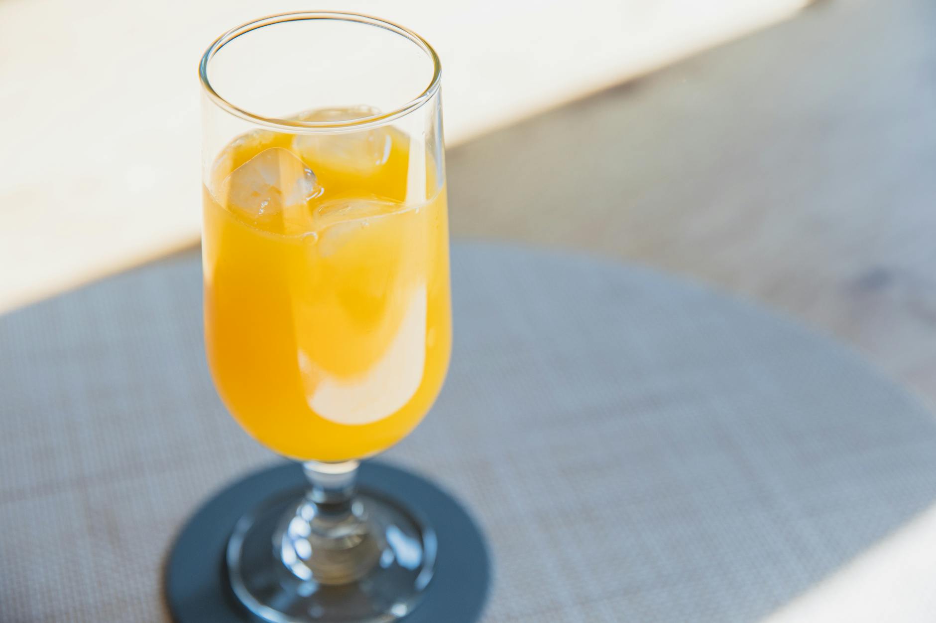 High angle of glass of orange juice with ice cubes placed on table