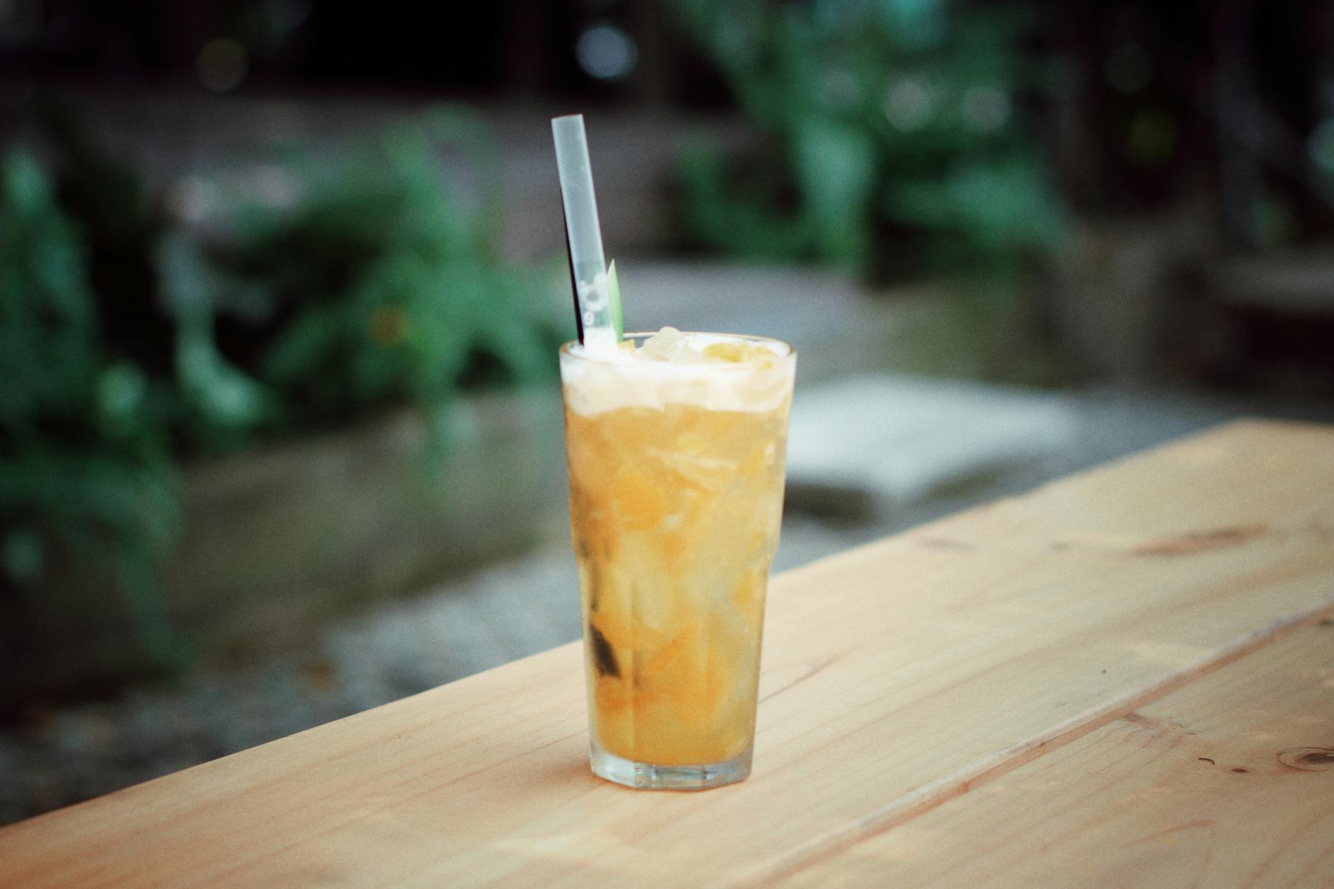 Chilled iced orange drink with straw on an outdoor wooden table. Refreshing and vibrant.