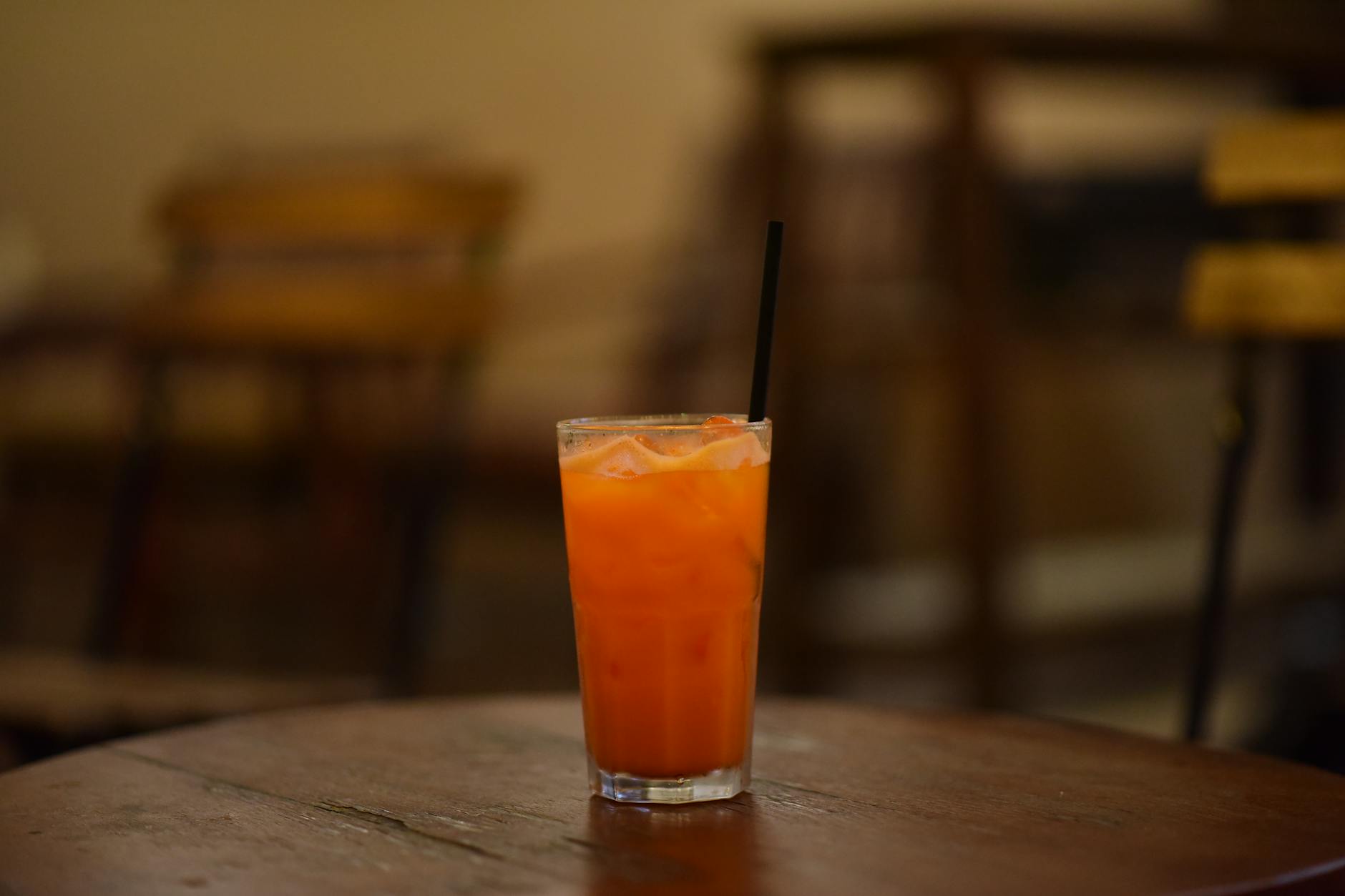 Glass of iced orange juice with a straw on wooden table in cozy cafe setting.