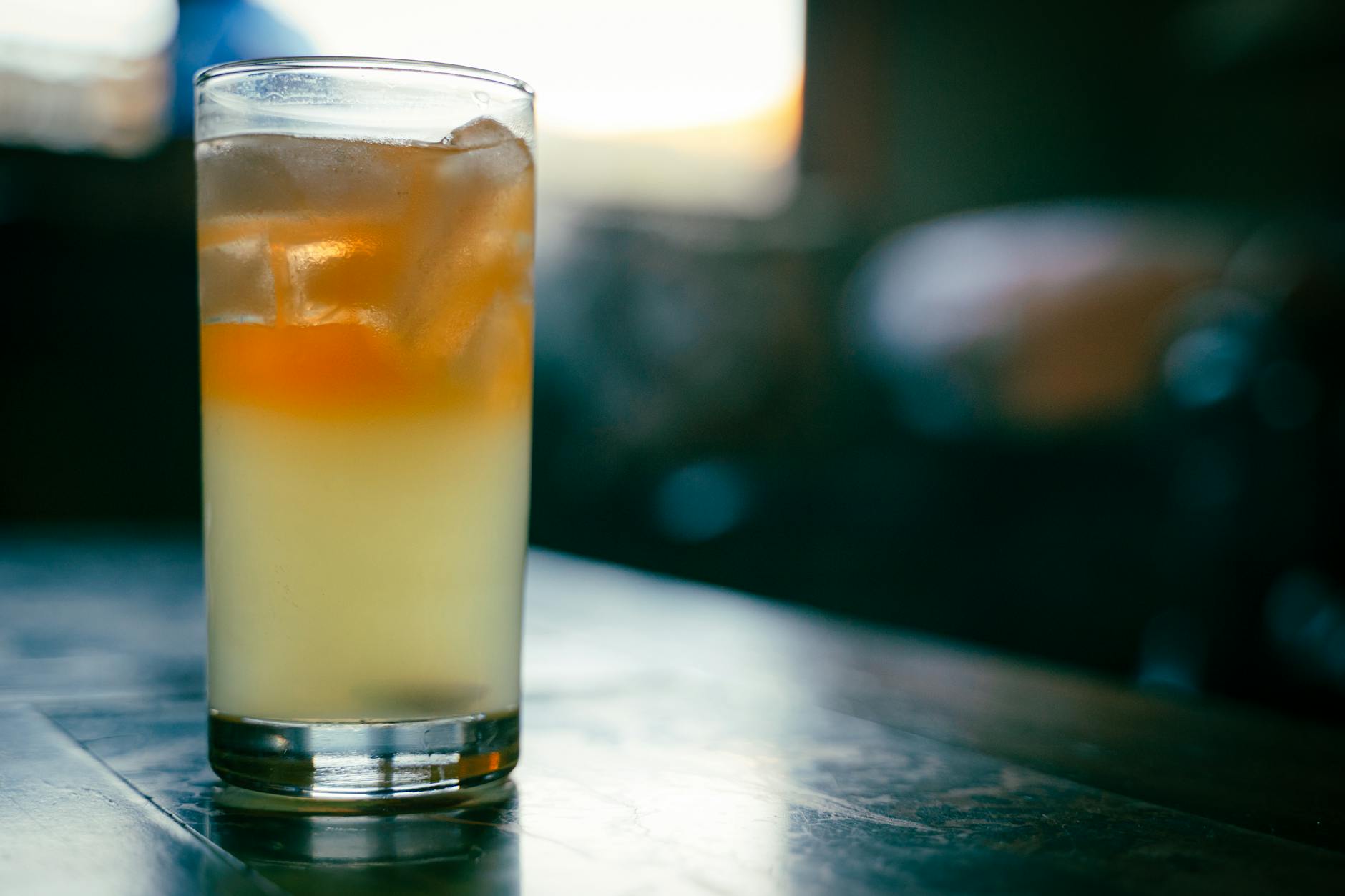 A glass of refreshing iced drink sits on a wooden table with a blurred background.