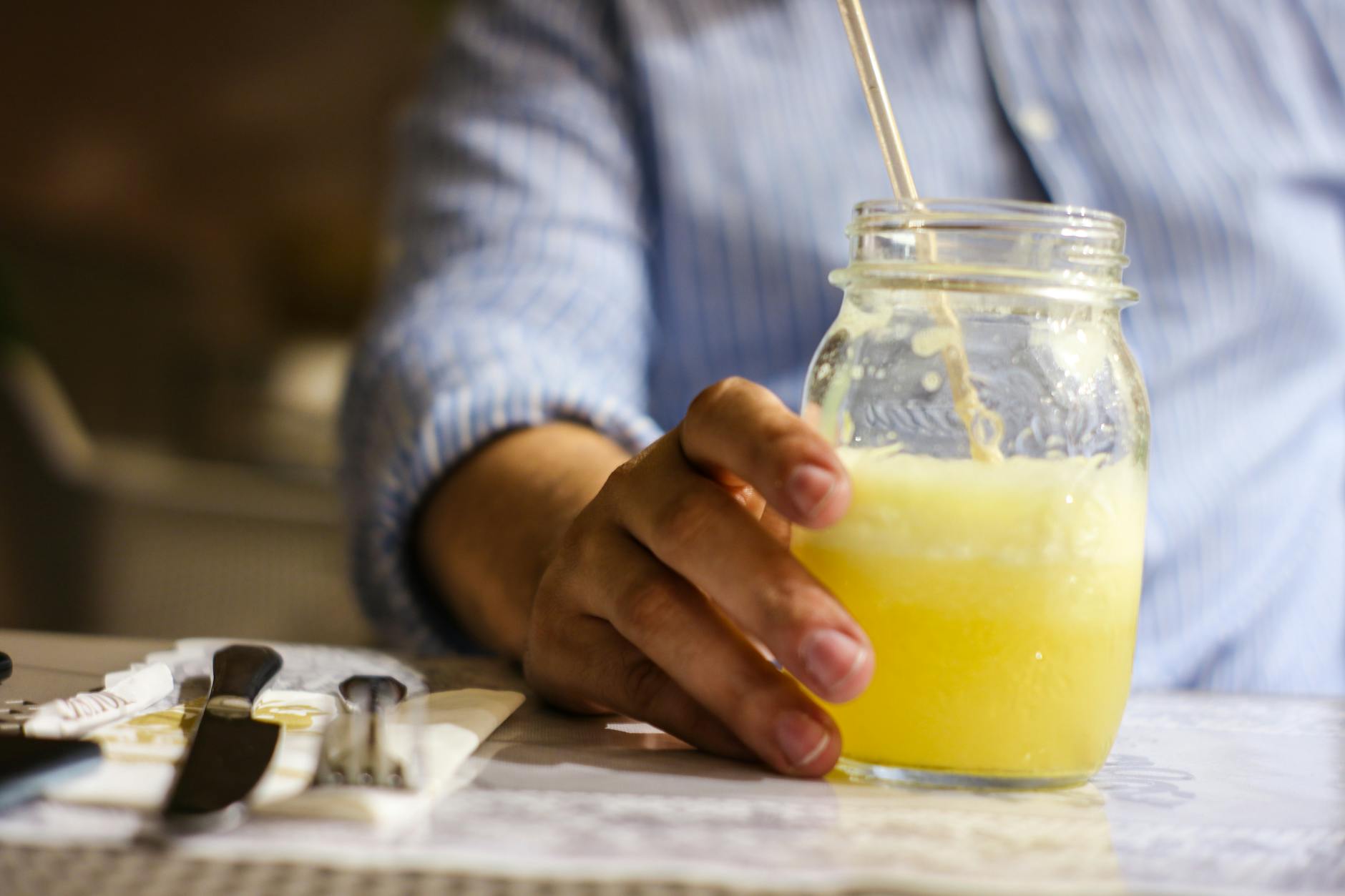 Person holding a refreshing glass jar of lemonade with a straw in an indoor setting.