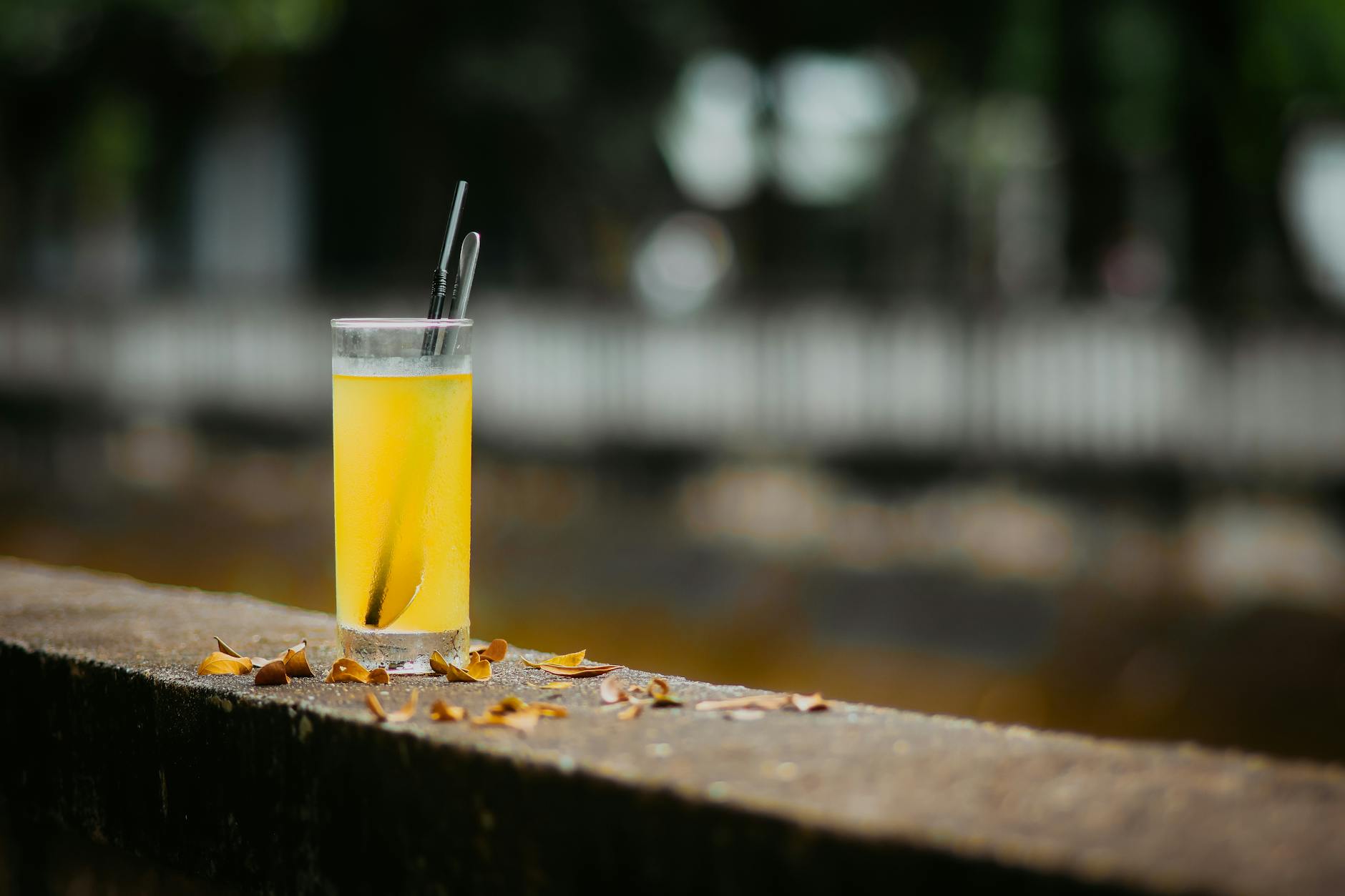A glass of lemon juice with straws on a ledge, outdoors in natural light.