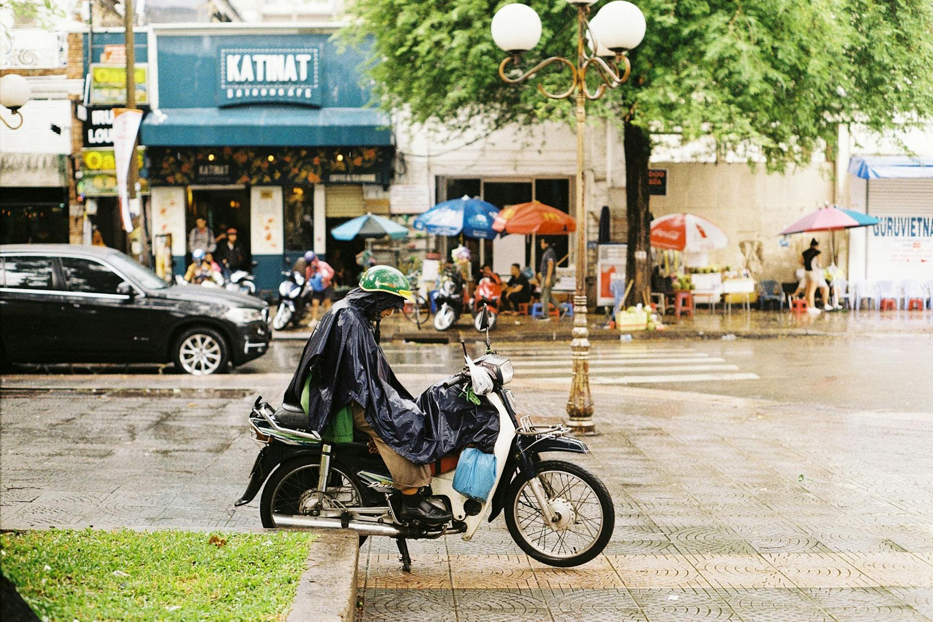 Motorcyclist in raincoat waits on street in Ho Chi Minh City, Vietnam.