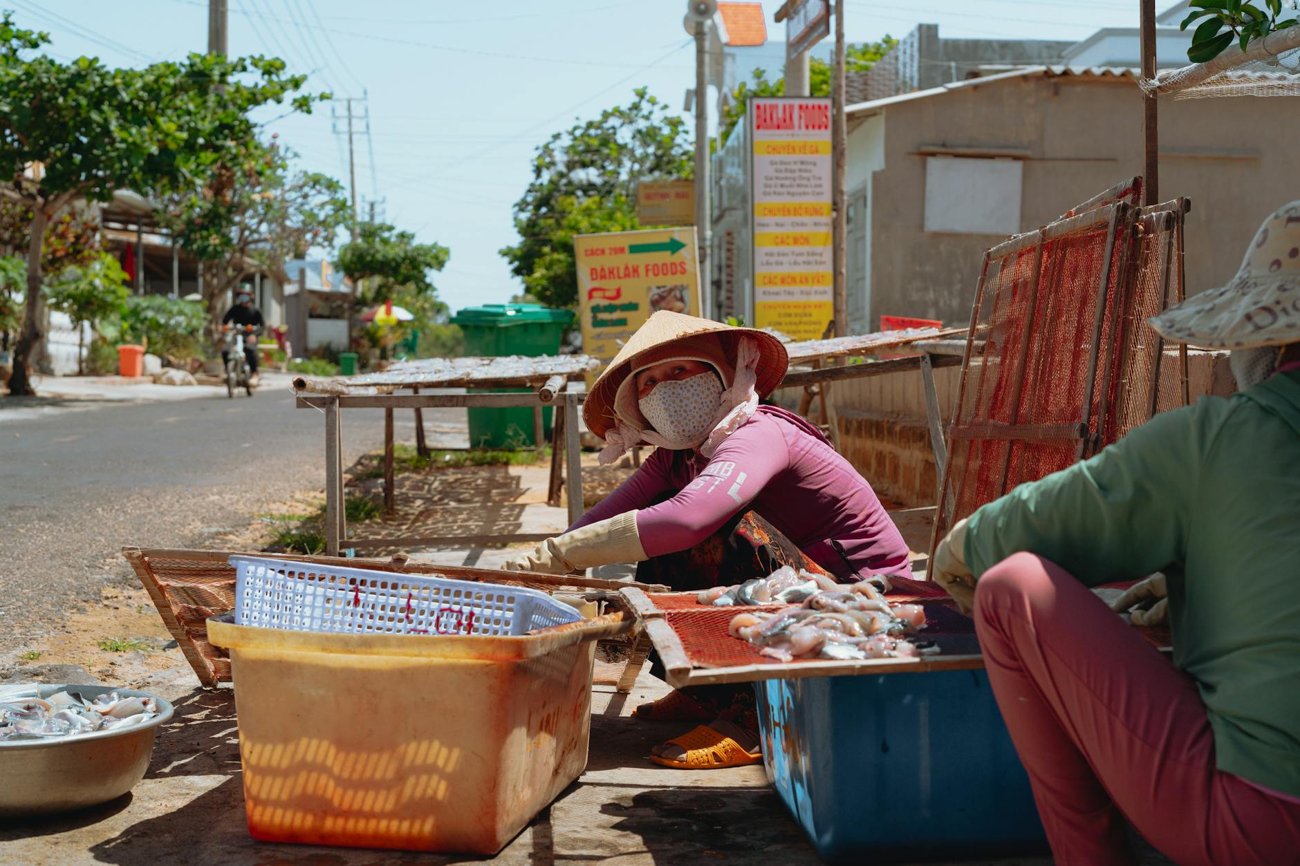 A street vendor in Bình Thuận, Vietnam dries seafood under the sun in a rural setting.