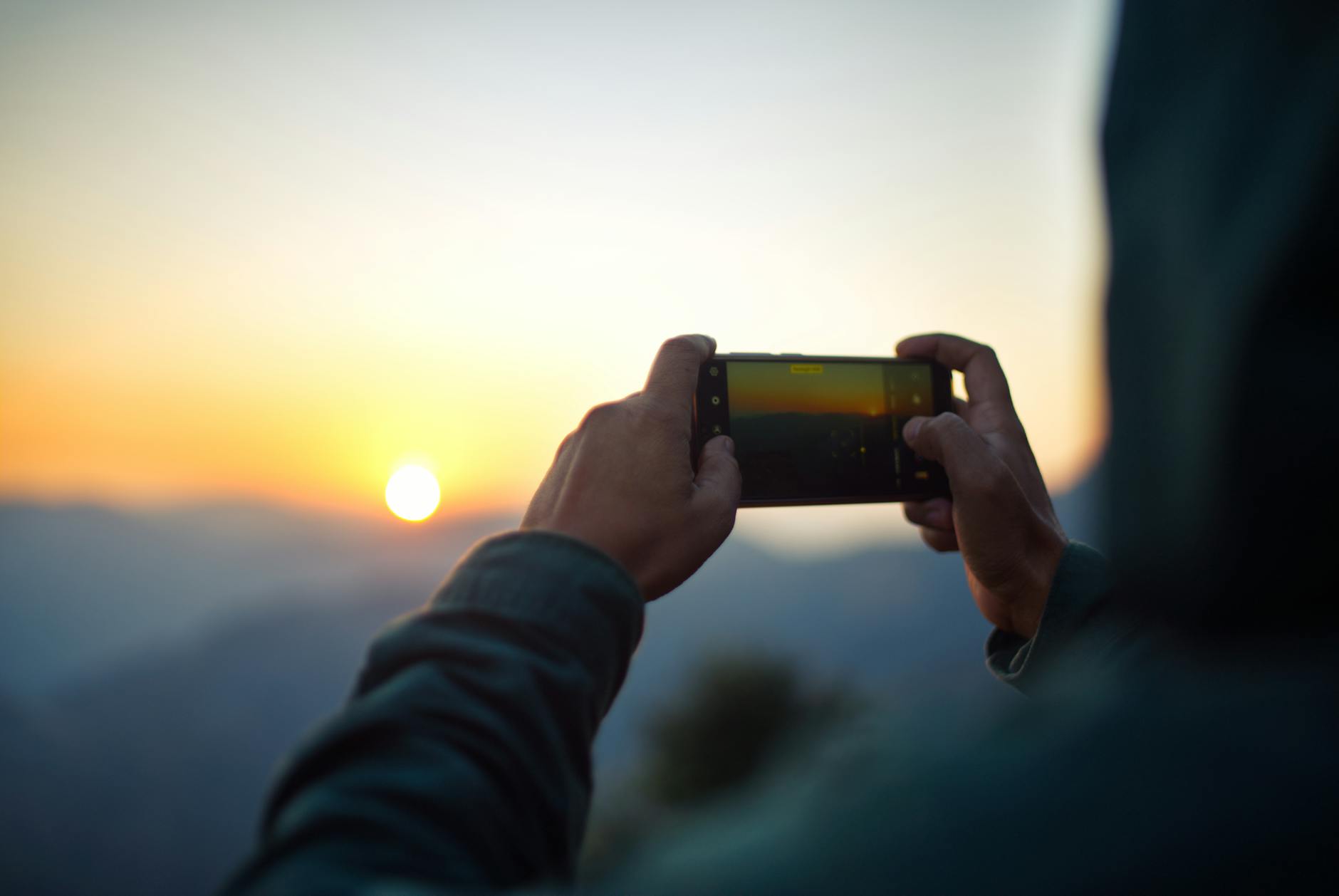 A person captures a stunning sunrise on a mobile phone, emphasizing outdoor photography and natural beauty.