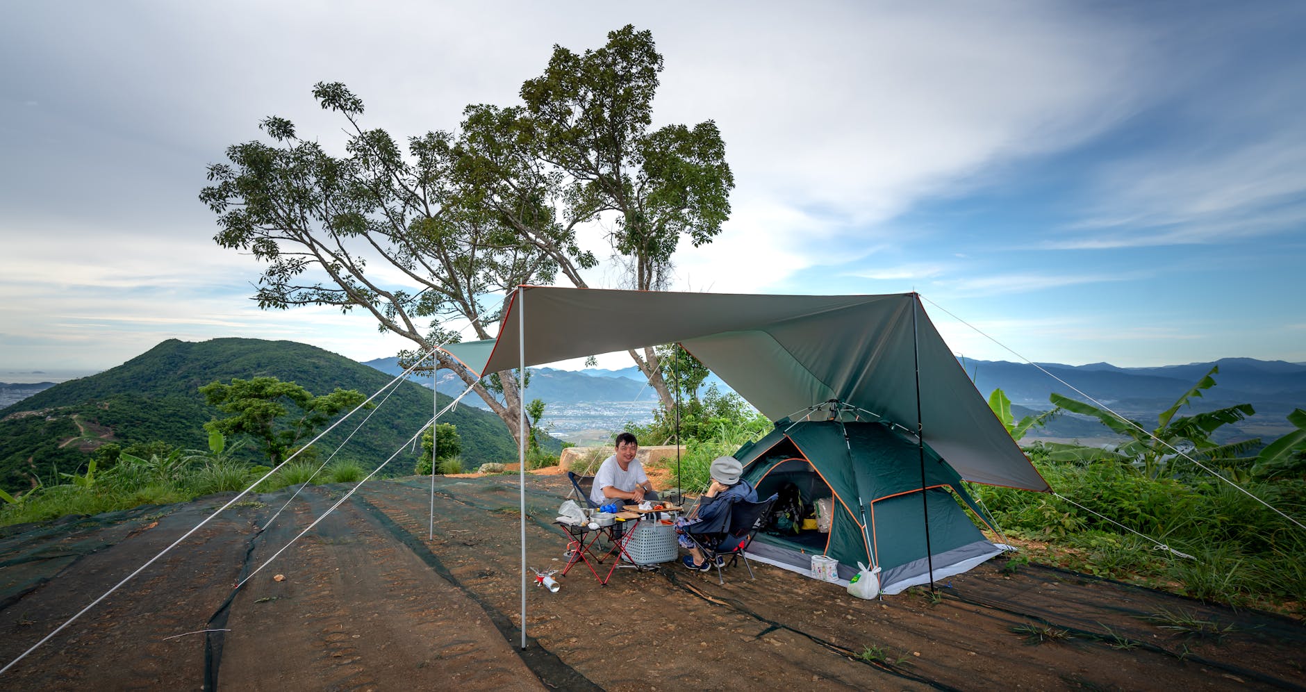 Outdoor camping scene with tent and tarp in a mountainous area during daytime.