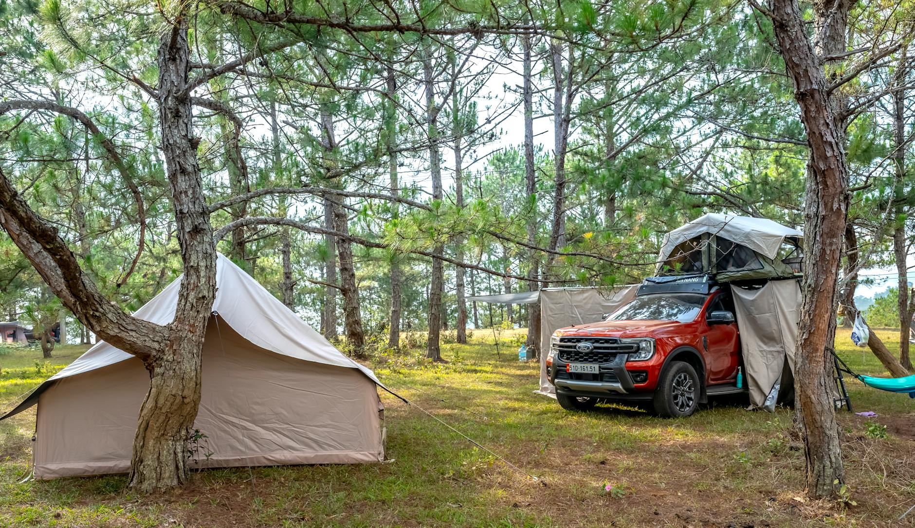 A peaceful camping scene with a tent and rooftop car tent in a lush forest setting.