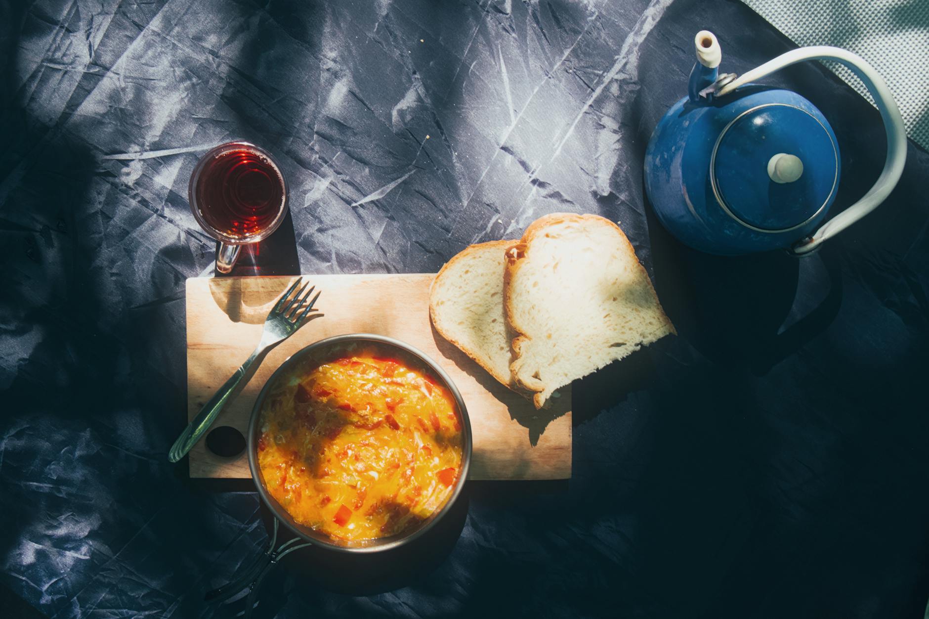 Sunny outdoor breakfast with omelette, bread, and tea setting.