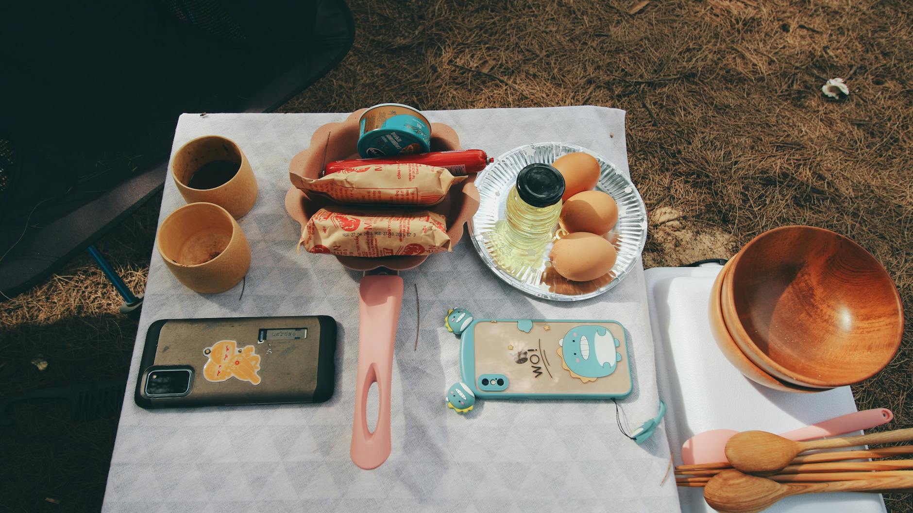 A top-down view of a picnic setup with snacks, eggs, utensils, and phones on an outdoor table.