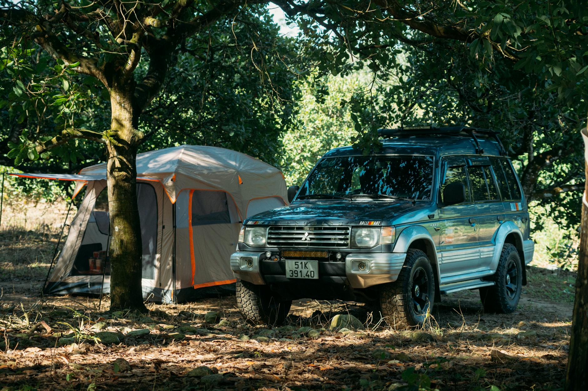 An SUV parked beside a tent in a forest, perfect for outdoor adventure enthusiasts.