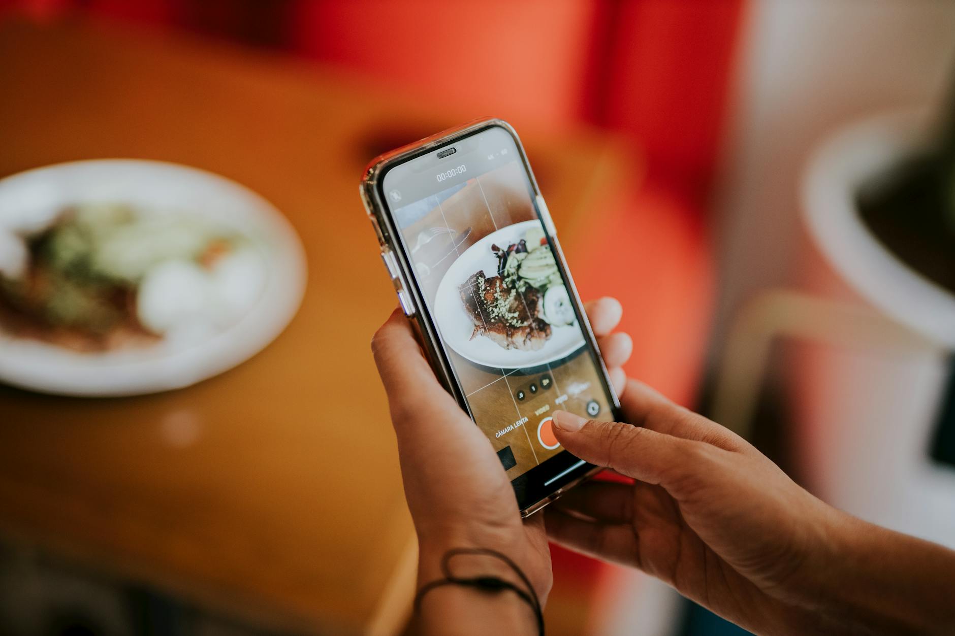 Close-up of a person using a smartphone to photograph food in a cozy indoor setting.
