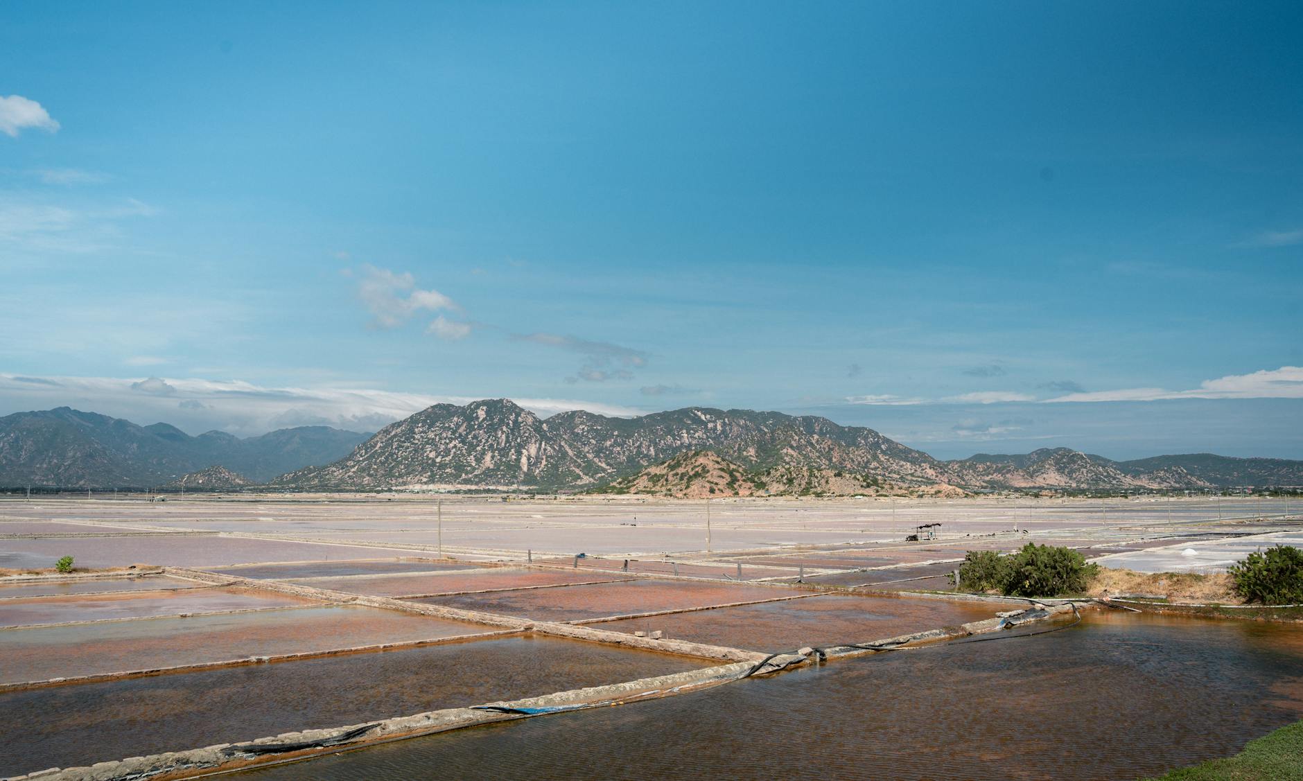 Vast scenic view of salt fields against a mountainous backdrop, clear blue sky above.