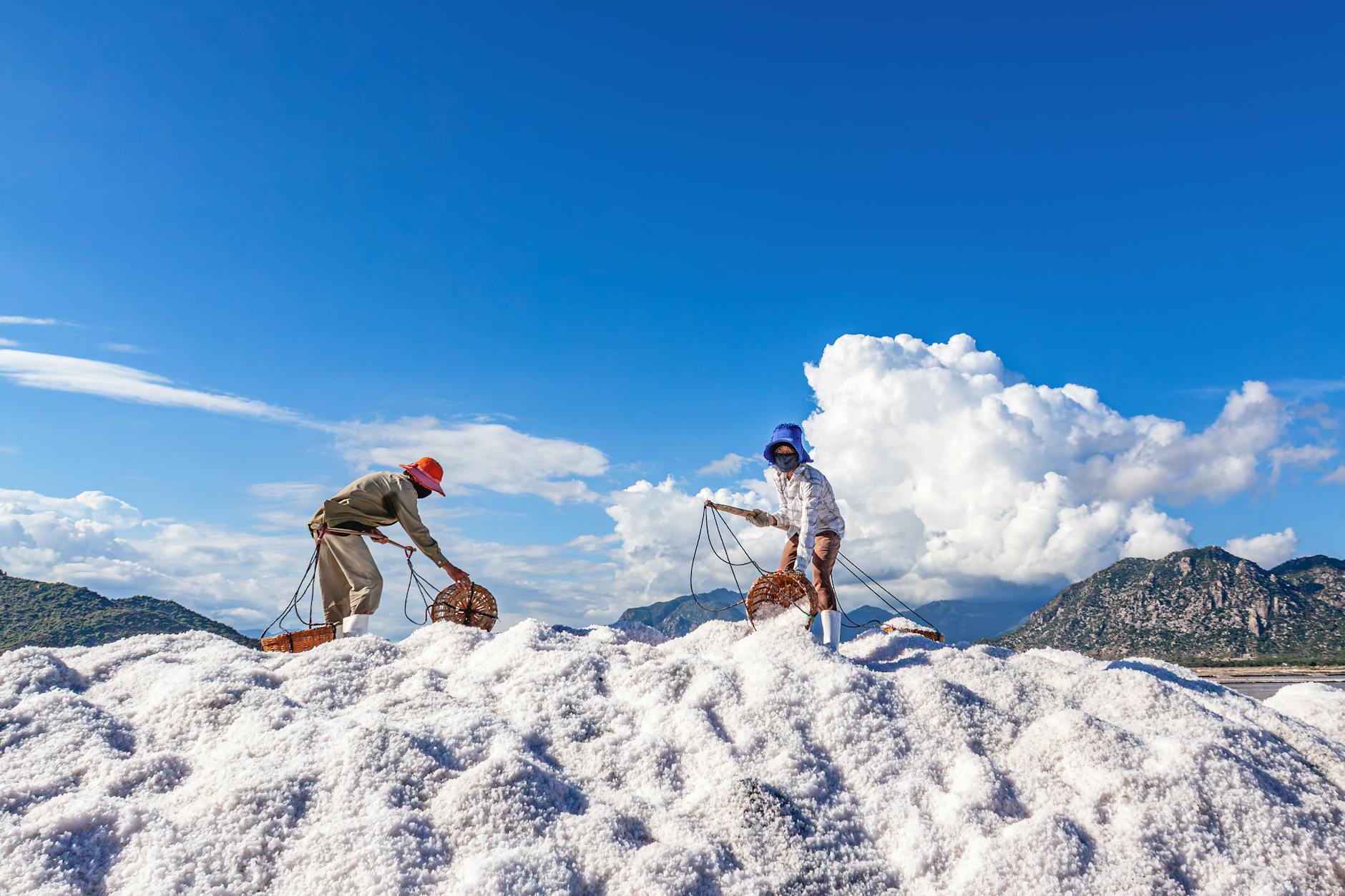 Salt farmers working on a salt field under a clear blue sky in Vietnam.
