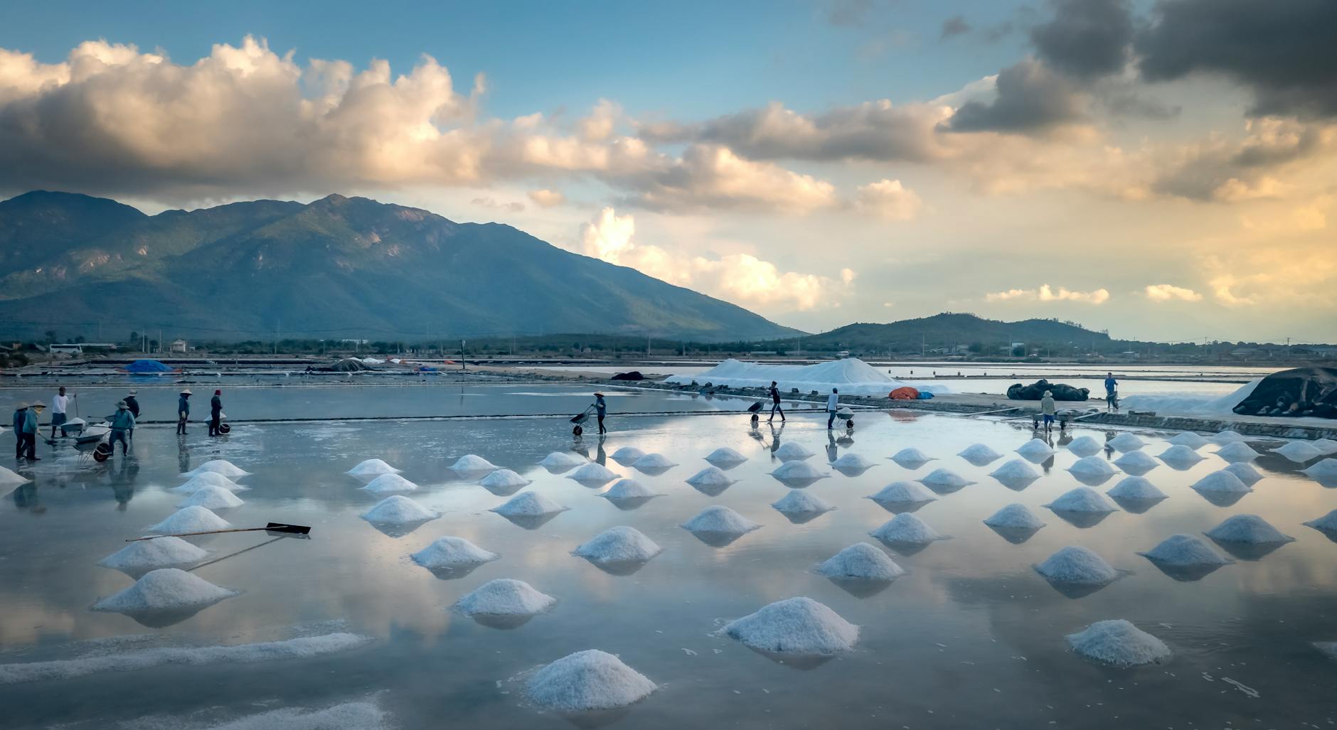 Laborers harvesting salt in scenic salt pans with mountains.