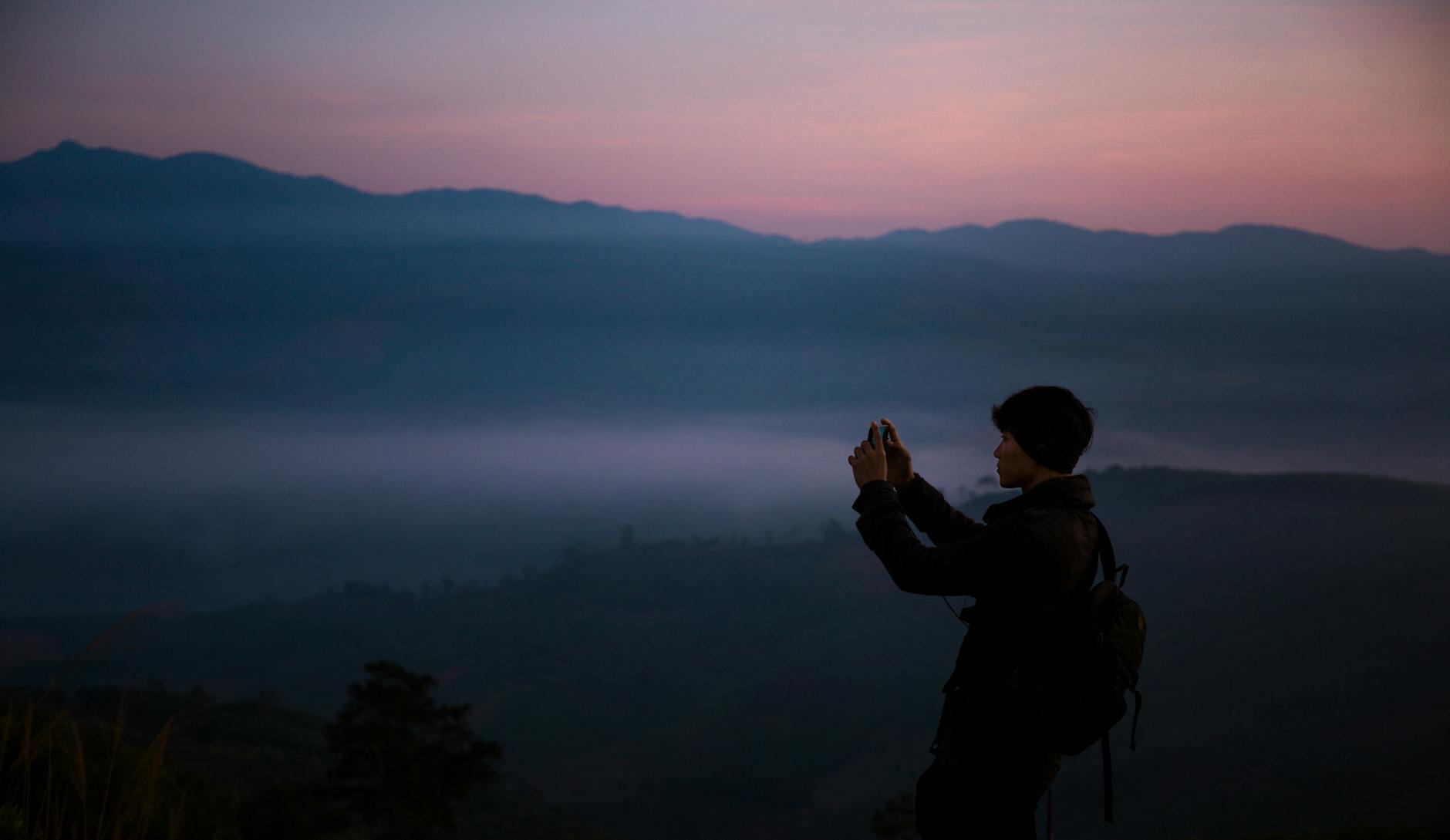 A hiker takes a photo during a serene mountain sunrise, capturing the beauty of nature.