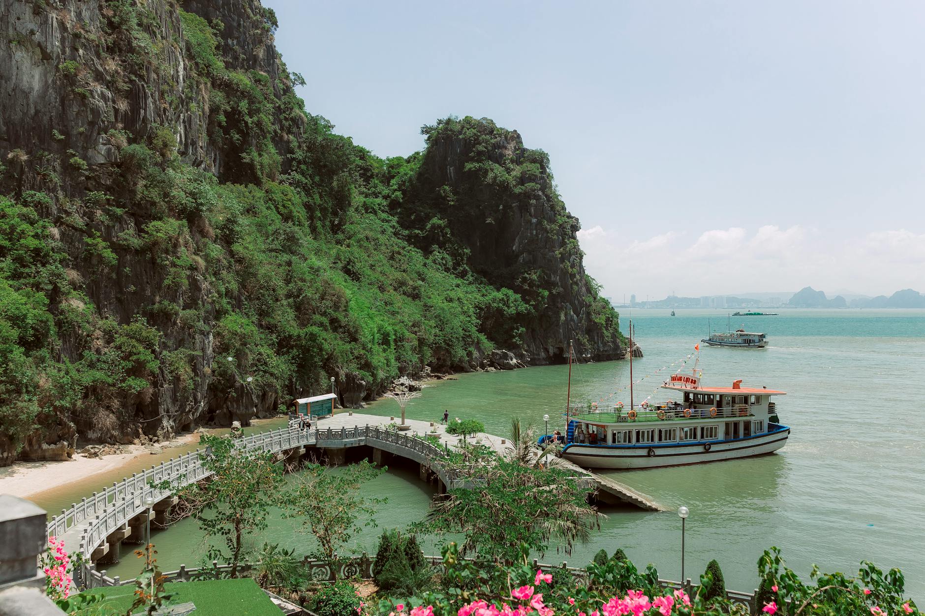 A picturesque view of boats near a scenic coastal bridge surrounded by lush greenery and towering cliffs.
