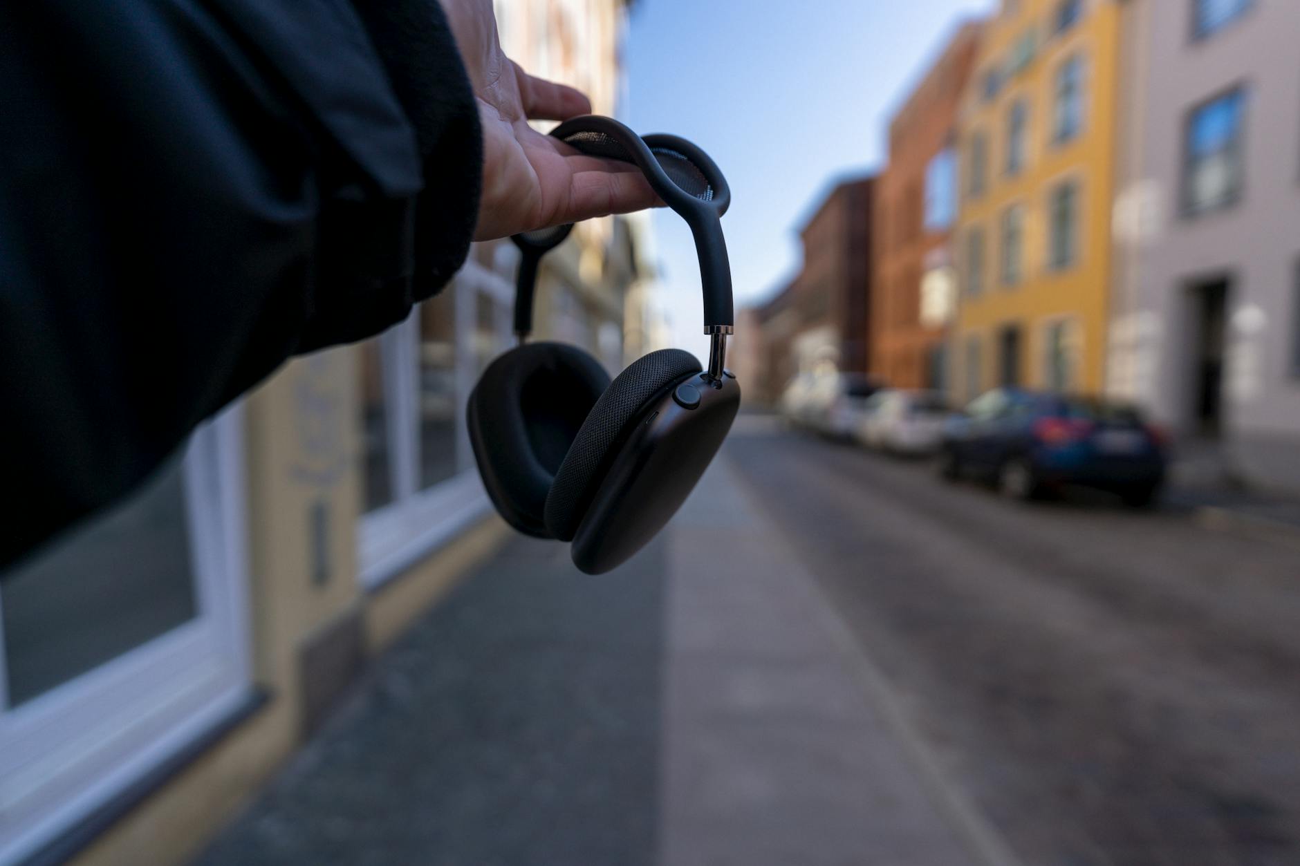 Close-up of a hand holding headphones in a city street setting with blurred background.