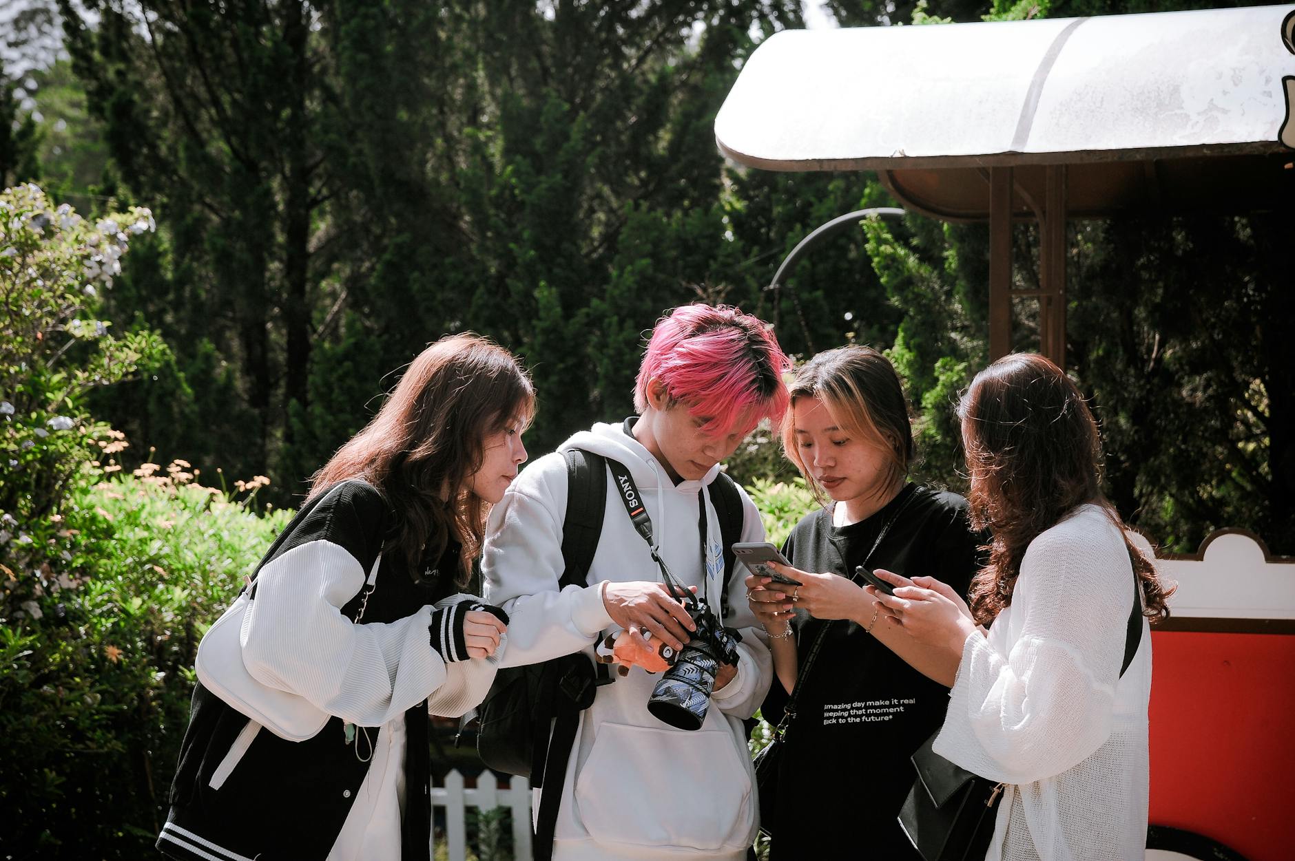 Group of teenagers using smartphones and a camera in a lush outdoor setting in Đà Lạt.