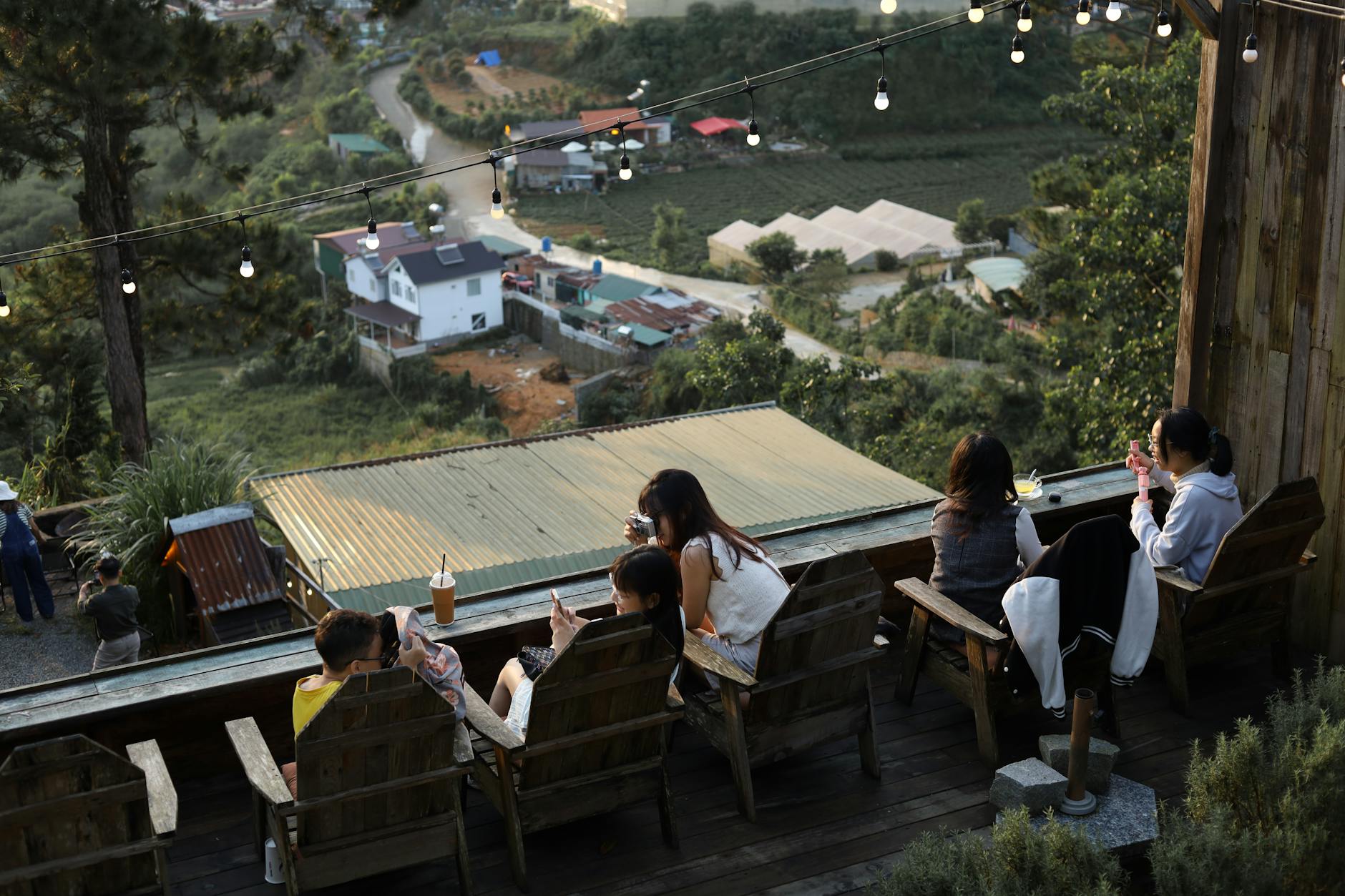 A group enjoys drinks on a terrace in Đà Lạt, Việt Nam, overlooking a lush village view.