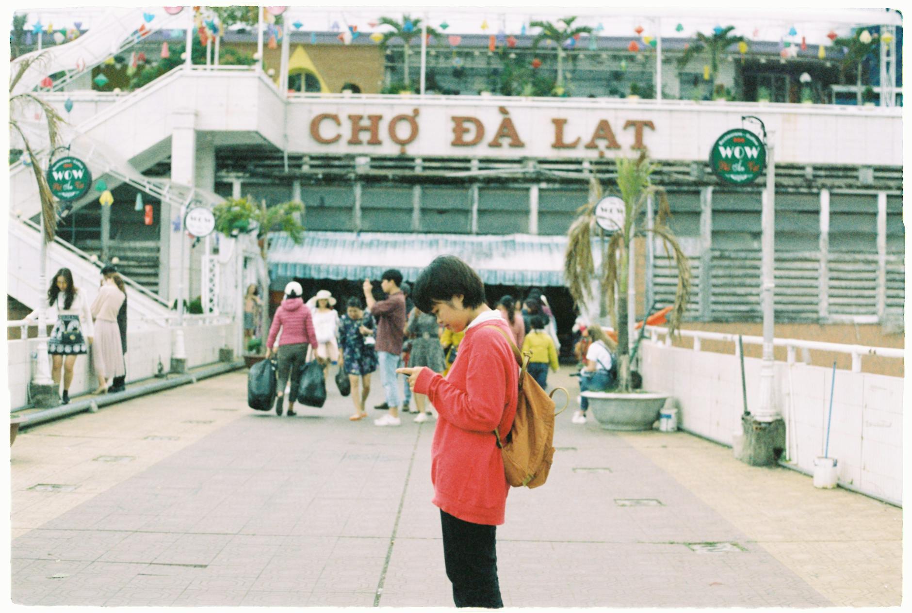 People walking and interacting at Chợ Đà Lạt market on a bright day.