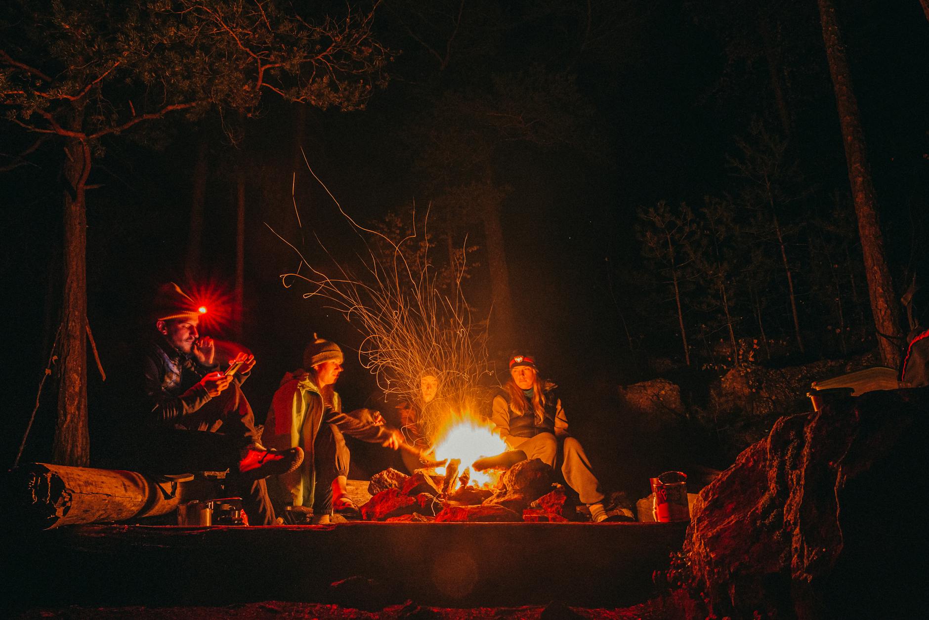 A group of adults enjoying a warm campfire during a night camping trip in the forest.
