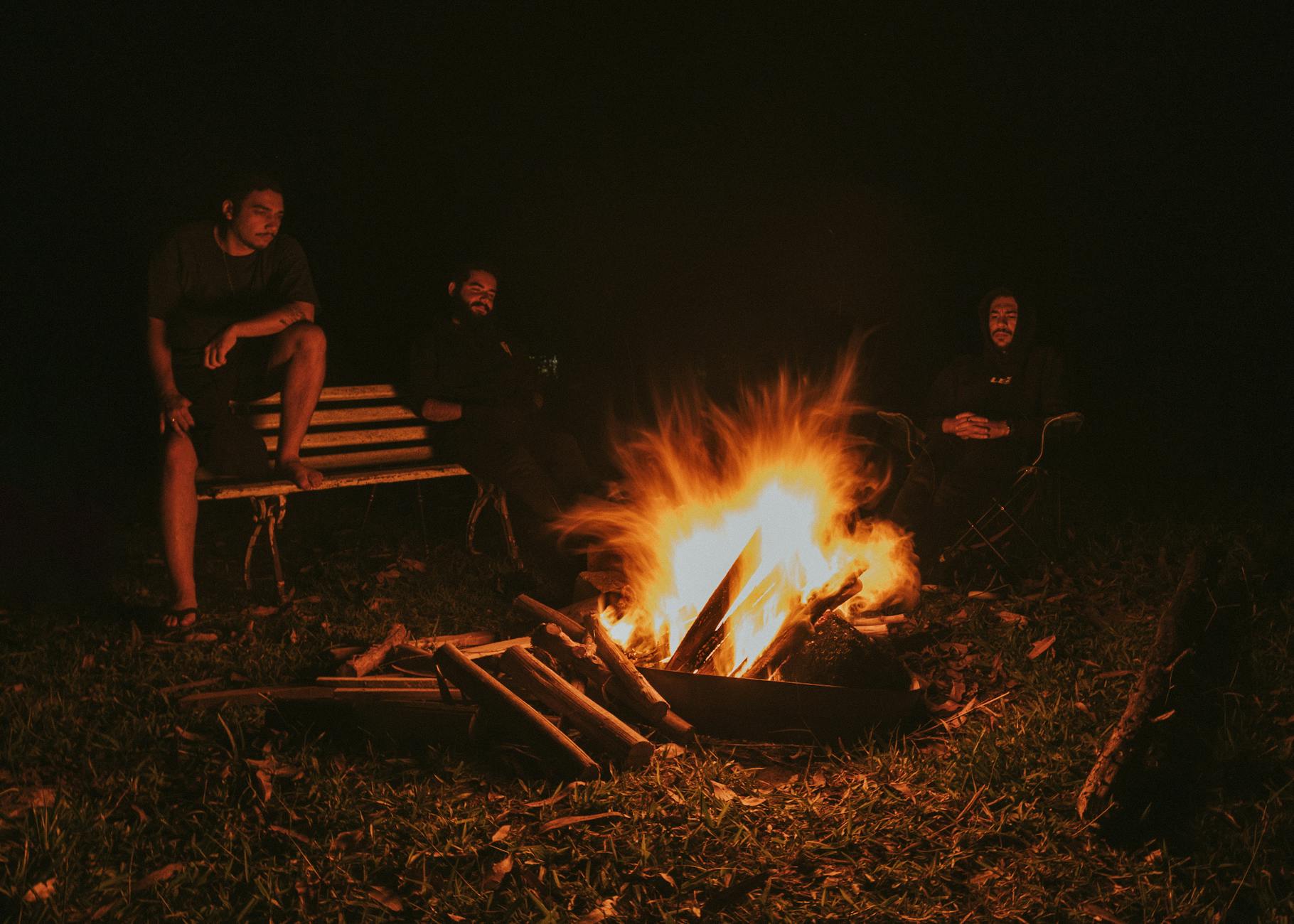 Men enjoying a warm bonfire in a dark outdoor setting, creating a cozy atmosphere.