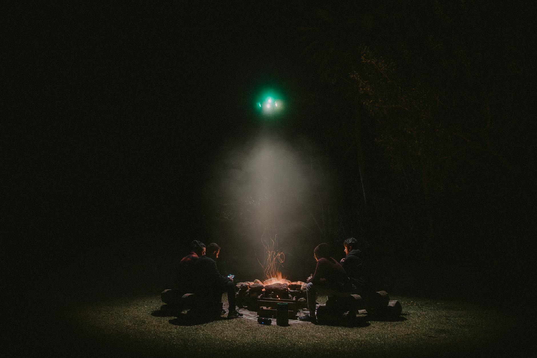 Friends enjoy a cozy campfire under the night sky in Brazil, highlighted by a drone's glow.