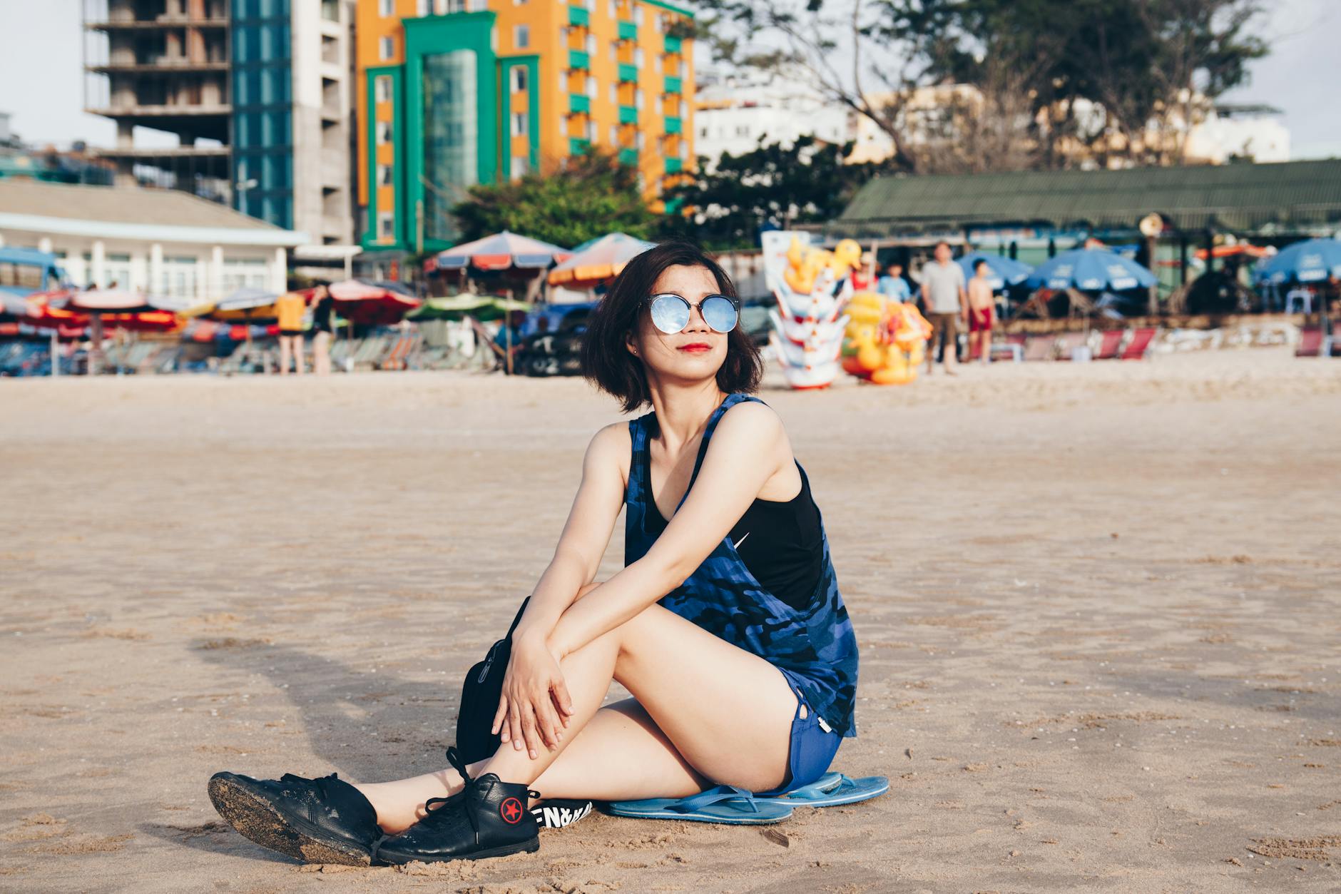 Woman sitting on a beach showcasing urban style with city backdrop.