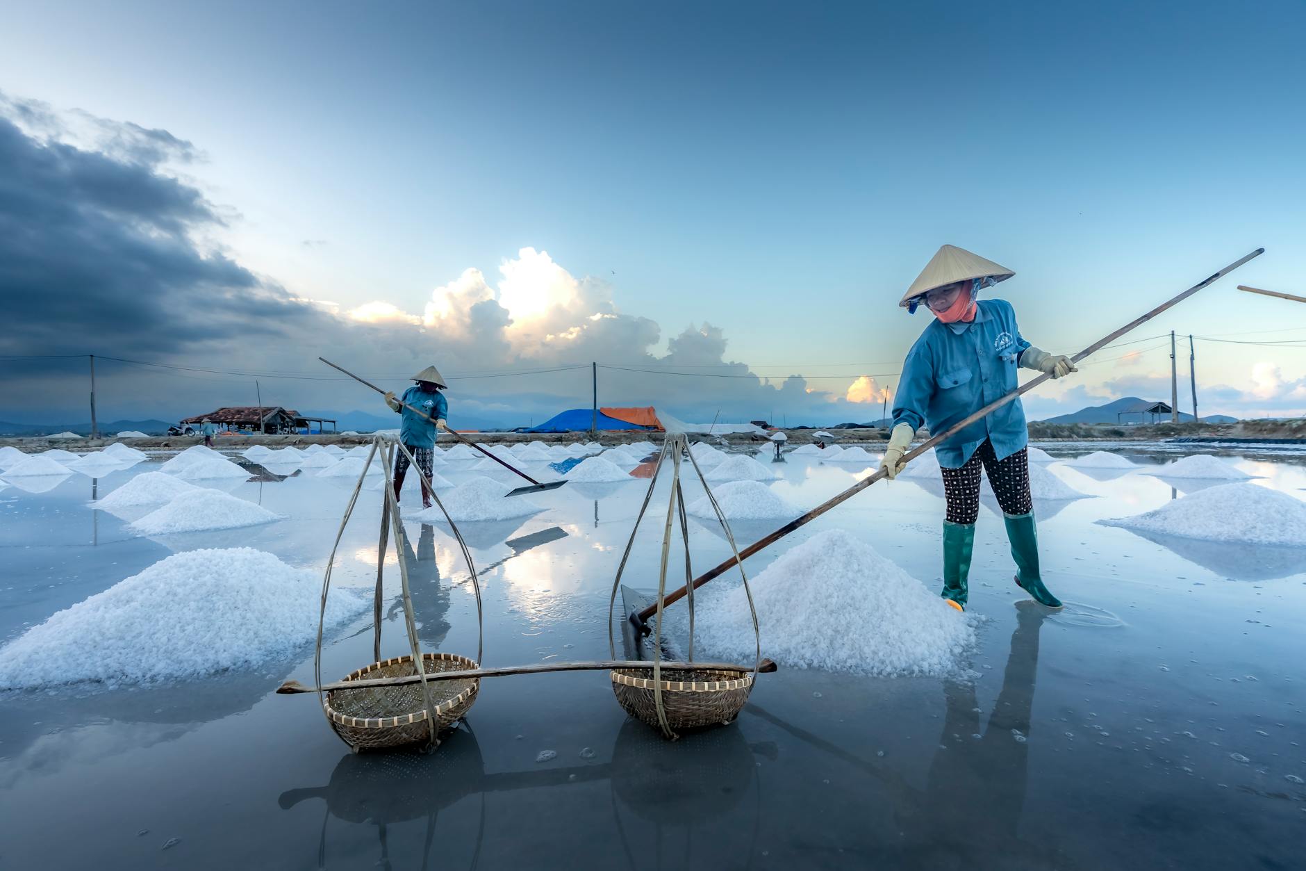 Salt farmers gathering salt in Vietnam's scenic salt flats at sunrise.