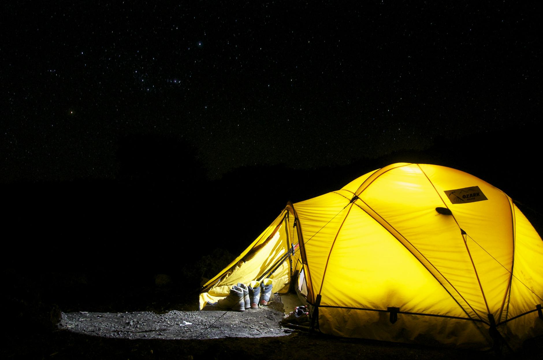 A glowing yellow tent pitched outdoors under a vast, star-filled night sky, capturing the essence of camping adventure.
