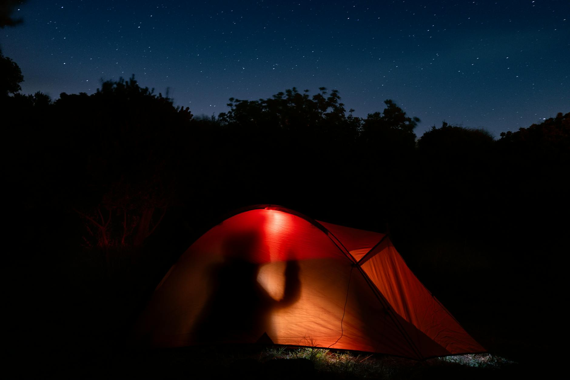 Silhouette camping under starry sky in Mudanya. A cozy illuminated tent amidst nature.