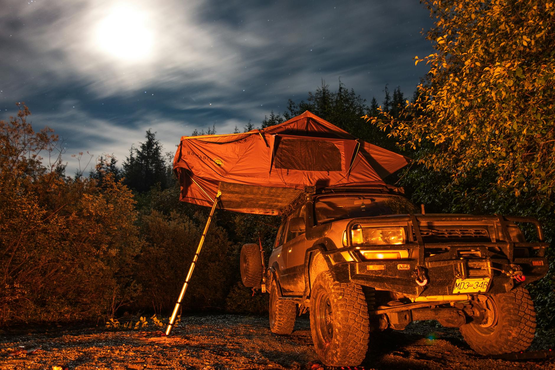 A night-time off-road camping scene with a jeep and rooftop tent under the moon.