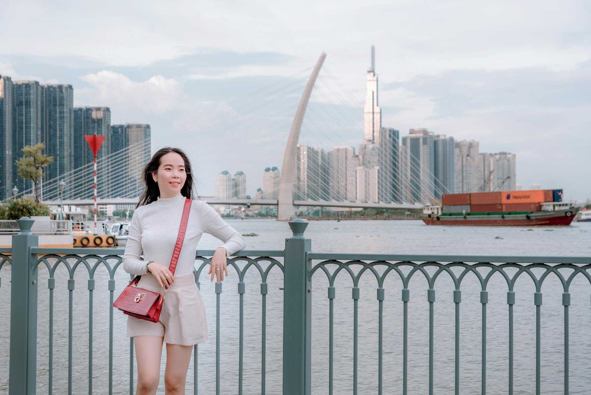 Asian woman leaning on railing by Thu Thiem 2 Bridge with city skyline, Vietnam.