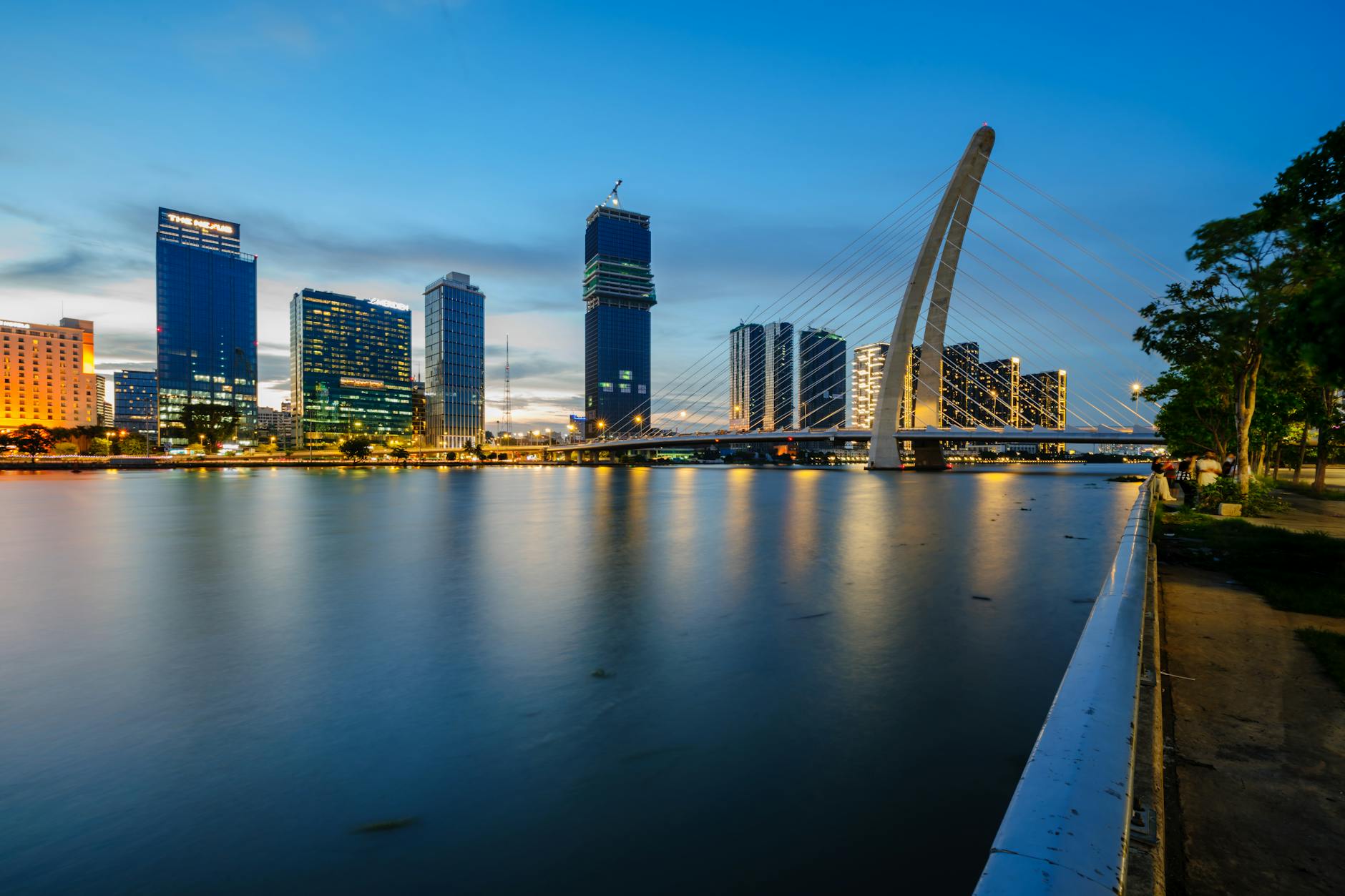 Beautiful view of modern city skyline and bridge reflecting in a calm river at twilight.