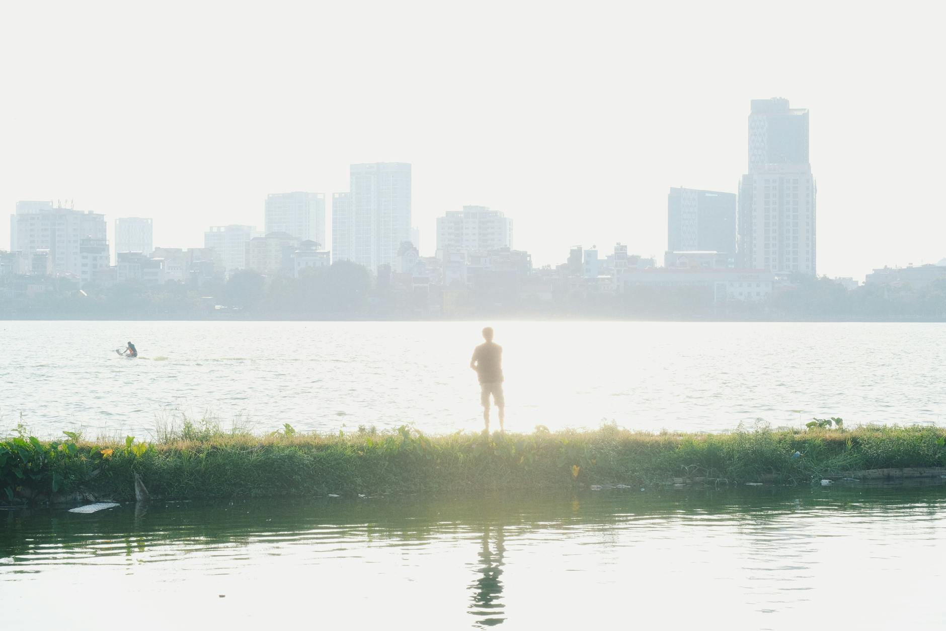 A silhouette of a person standing by Tây Hồ Lake with Hanoi skyline at sunrise.