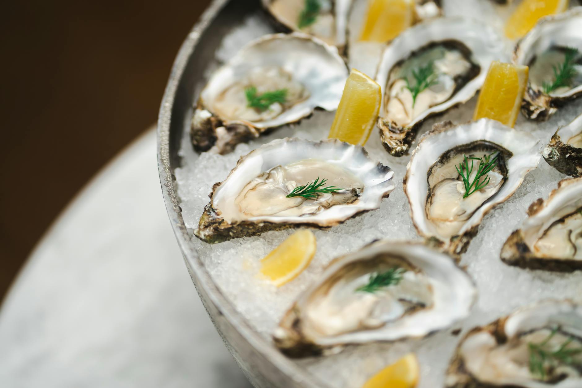 Gourmet platter of fresh oysters on ice with lemon and dill garnish in a restaurant setting.