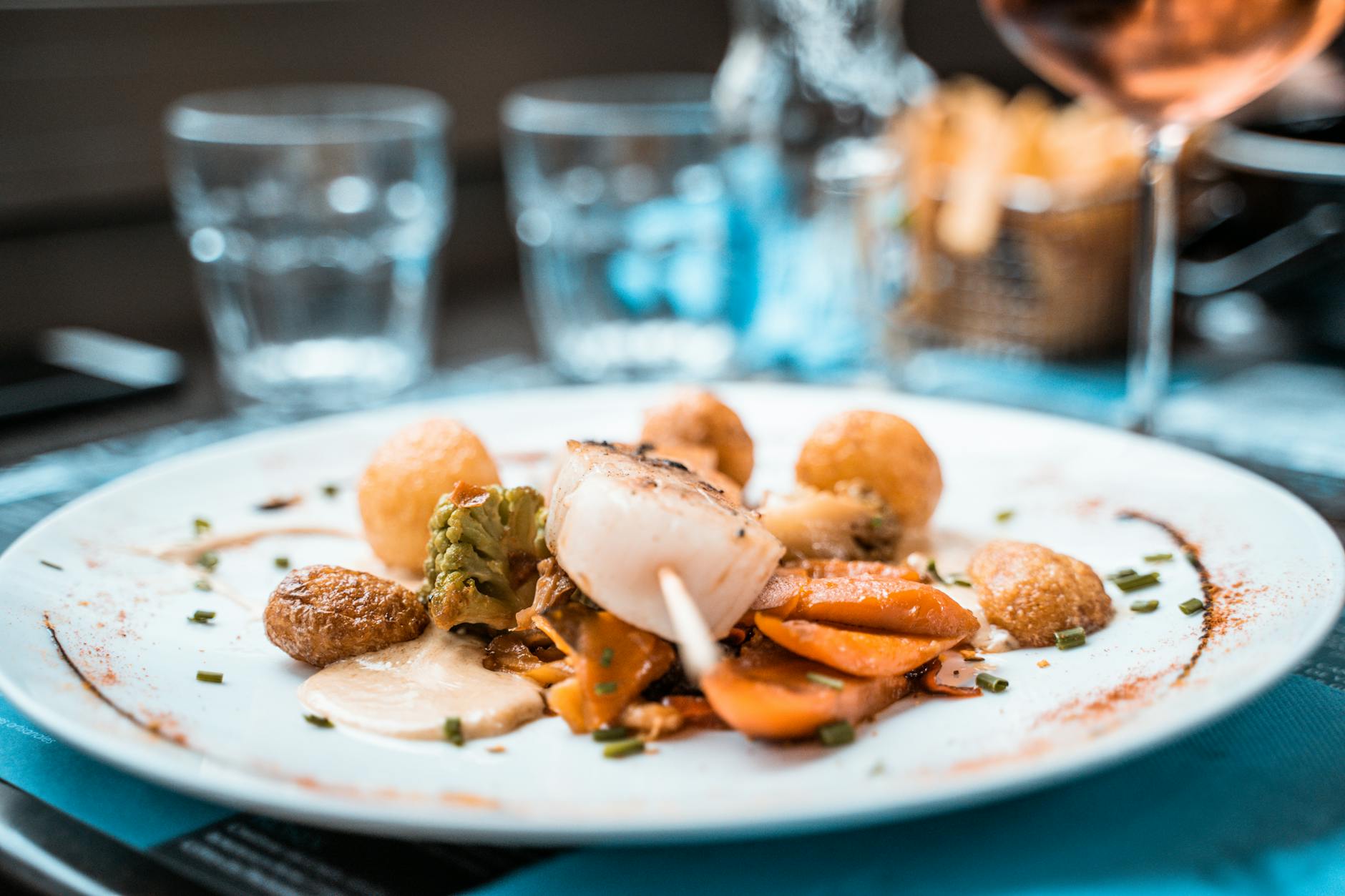 Beautifully plated scallop dish with vegetables and fries in a French restaurant setting.